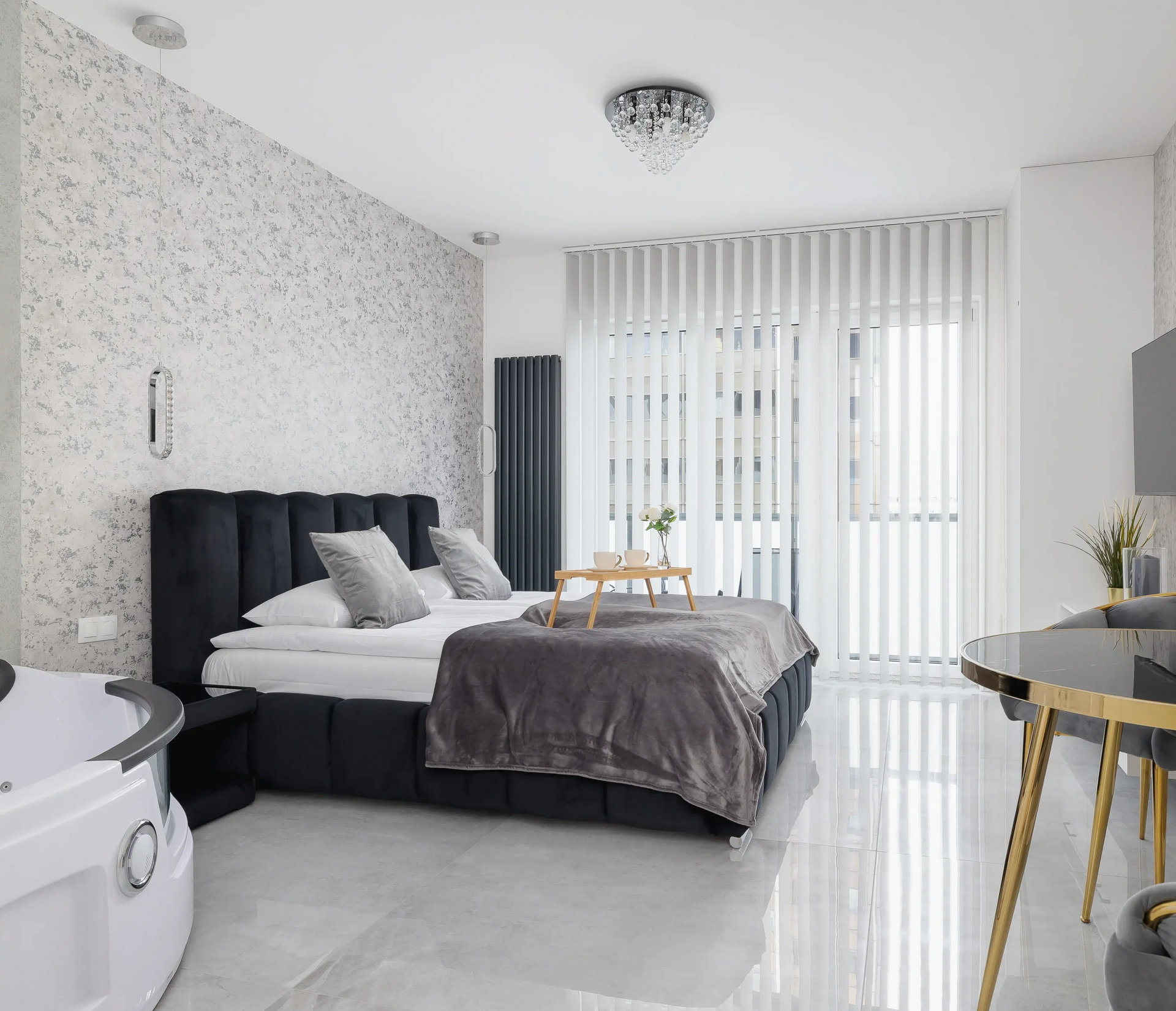 Nowoczesna sypialnia z łóżkiem, jacuzzi i dużym oknem z żaluzjami pionowymi.