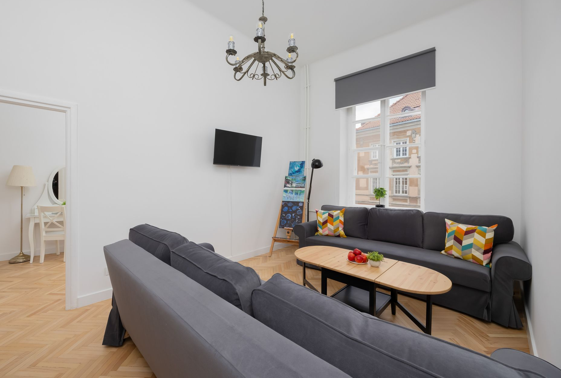 Salon z szarymi sofami, telewizorem, dziełami sztuki, oknem i małym stolikiem.