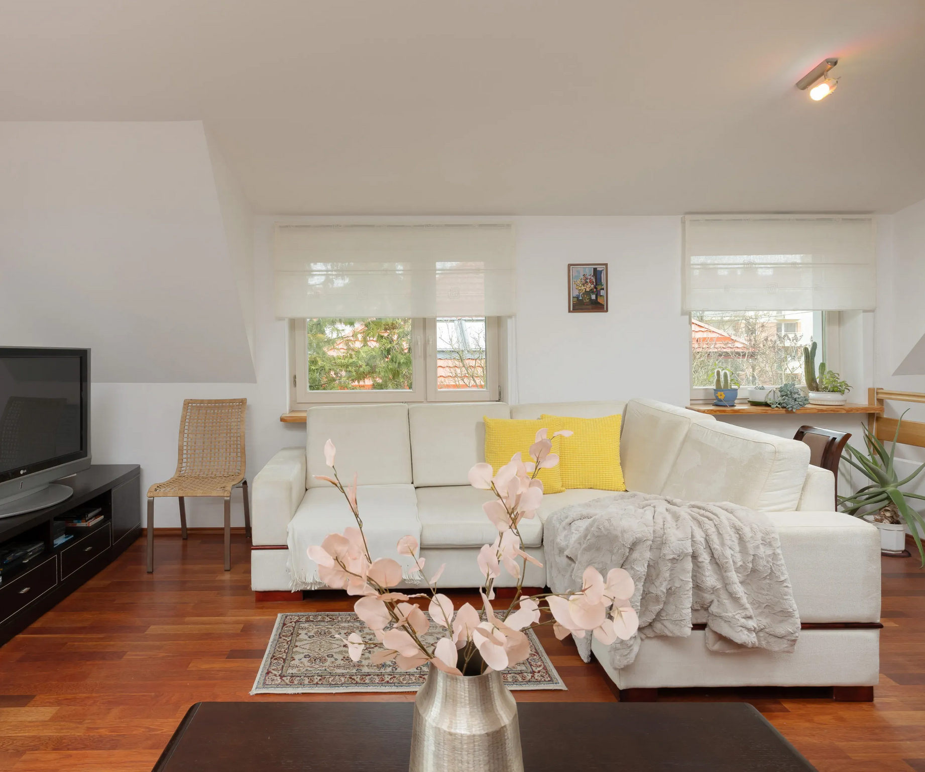 Salon z białą sofą modułową, telewizorem i drewnianą podłogą. Jasny, z oknem.