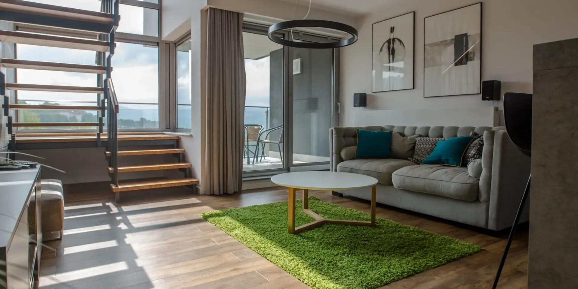 Nowoczesny salon z zielonym dywanem, szarą sofą i schodami prowadzącymi do okna z widokiem.