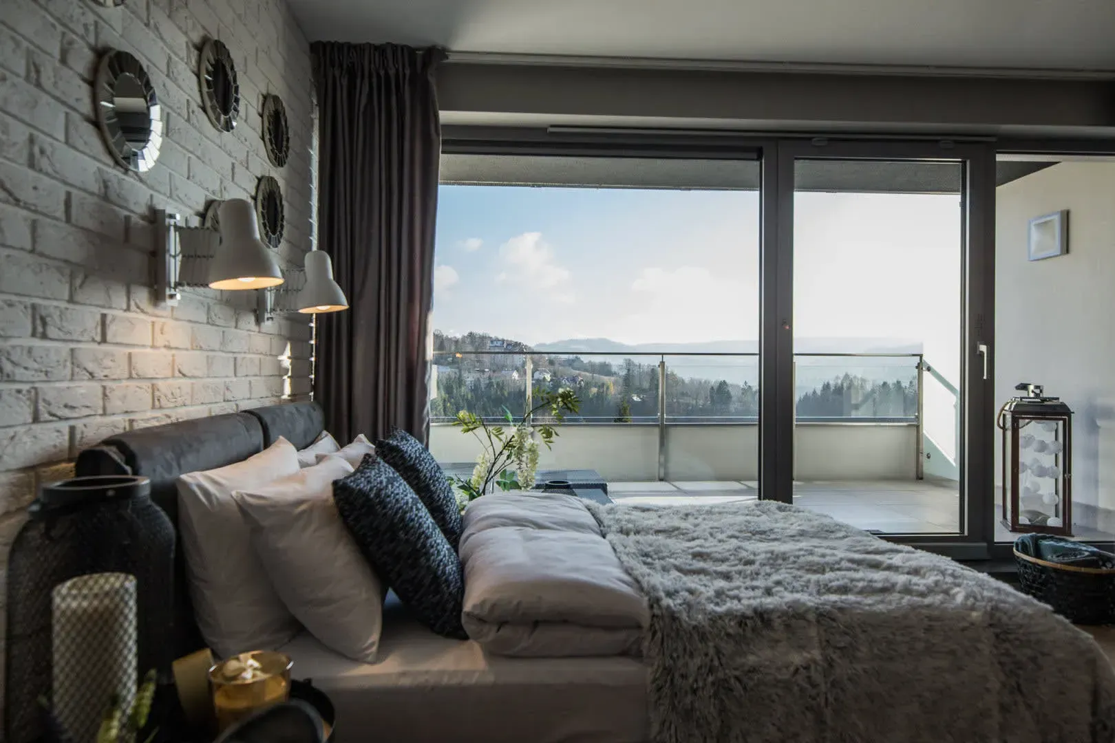 Sypialnia z białą ceglaną ścianą, dużym oknem z widokiem na malowniczy widok i łóżkiem z miękką pościelą.