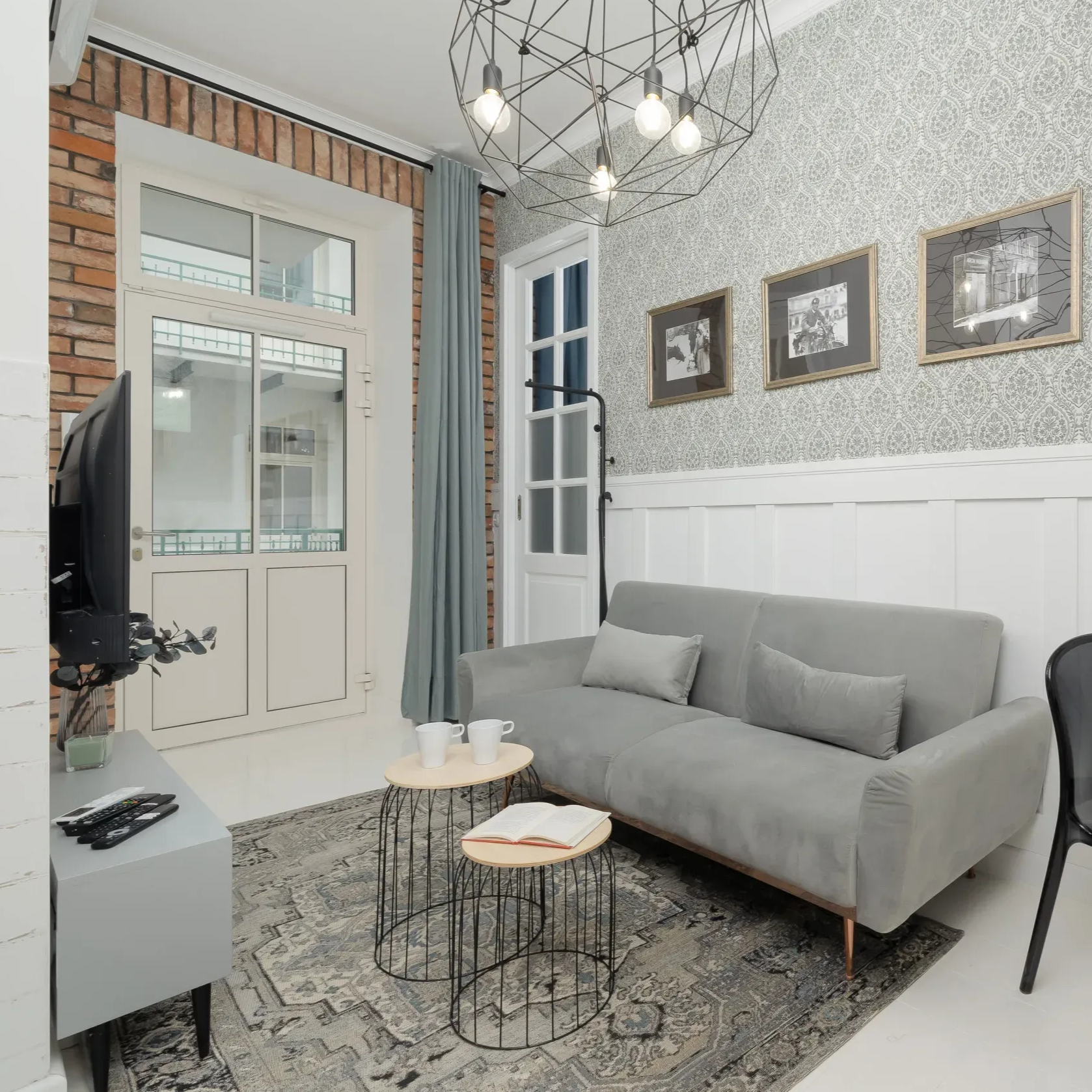 Przytulny salon z szarą sofą, stolikami kawowymi, dywanem, ceglaną ścianą i dekoracyjną tapetą.