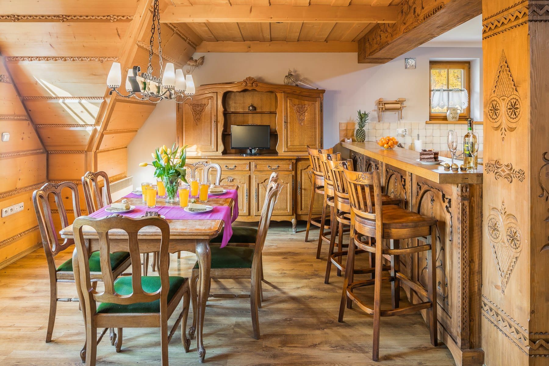 Drewniany kącik jadalny ze stołem, krzesłami barowymi i dekoracyjną szafką.