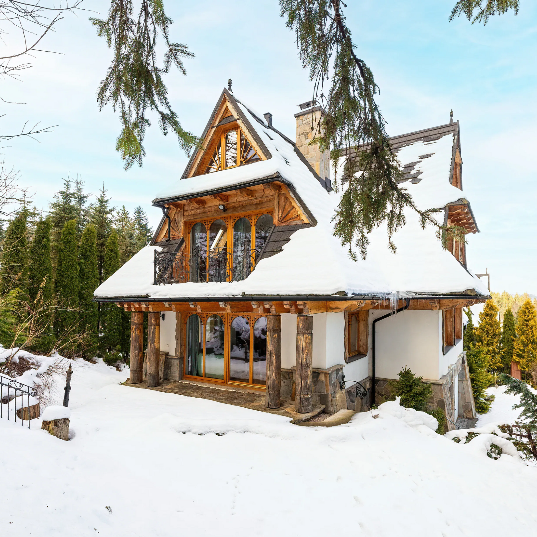 Pokryta śniegiem drewniana chata z dużymi oknami i spiczastym dachem w otoczeniu zimowego lasu.