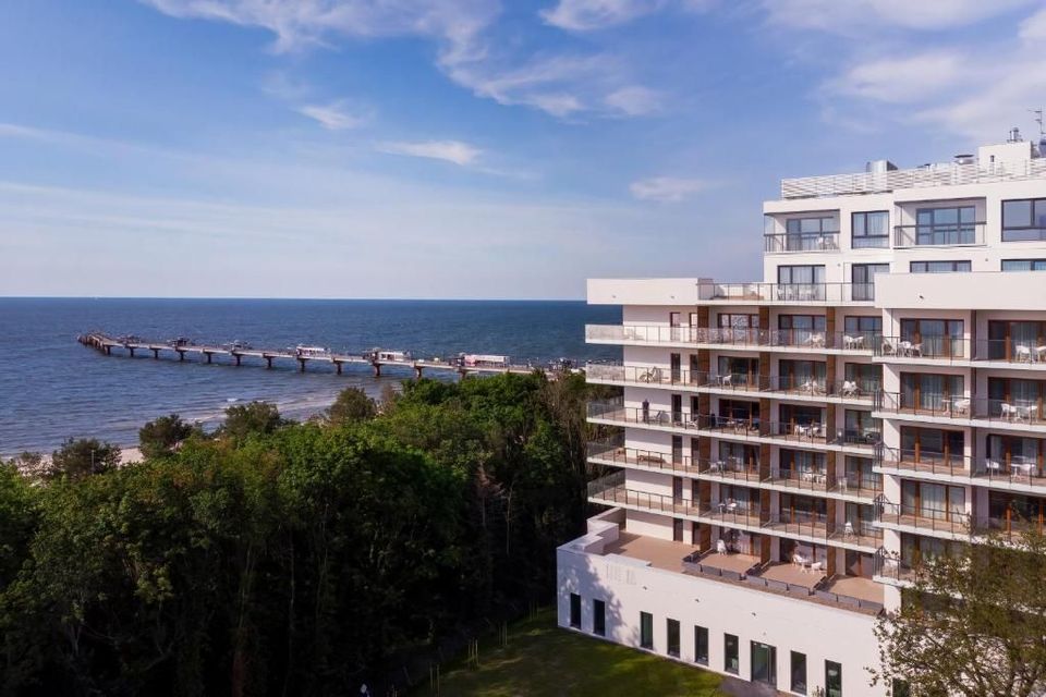 Hotel nadmorski z widokiem na ocean pod błękitnym niebem, z falochronem i zielenią na pierwszym planie