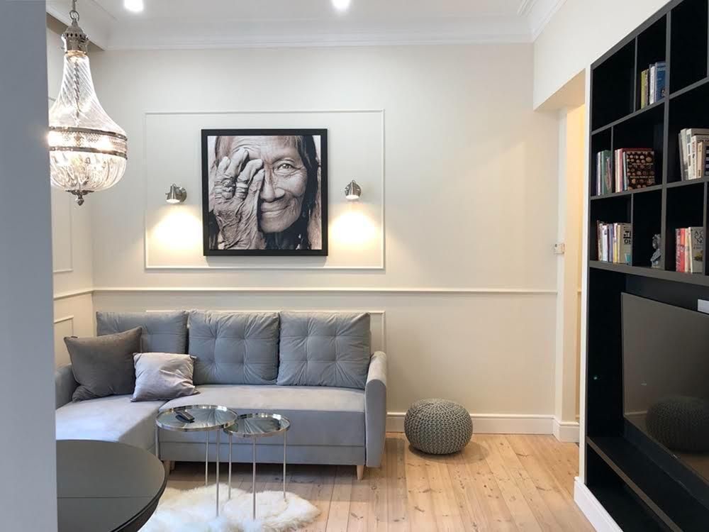 Przytulny salon z szarą sofą modułową, czarną półką ścienną i oprawionym portretem nad sofą w ciepłym oświetleniu.