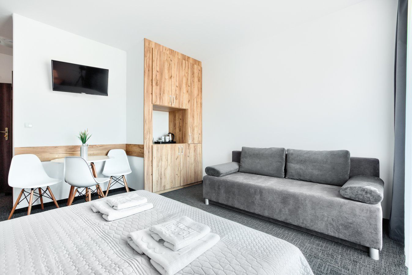 Pokój hotelowy z szarą sofą, łóżkiem z białą pościelą, krzesłami i telewizorem.