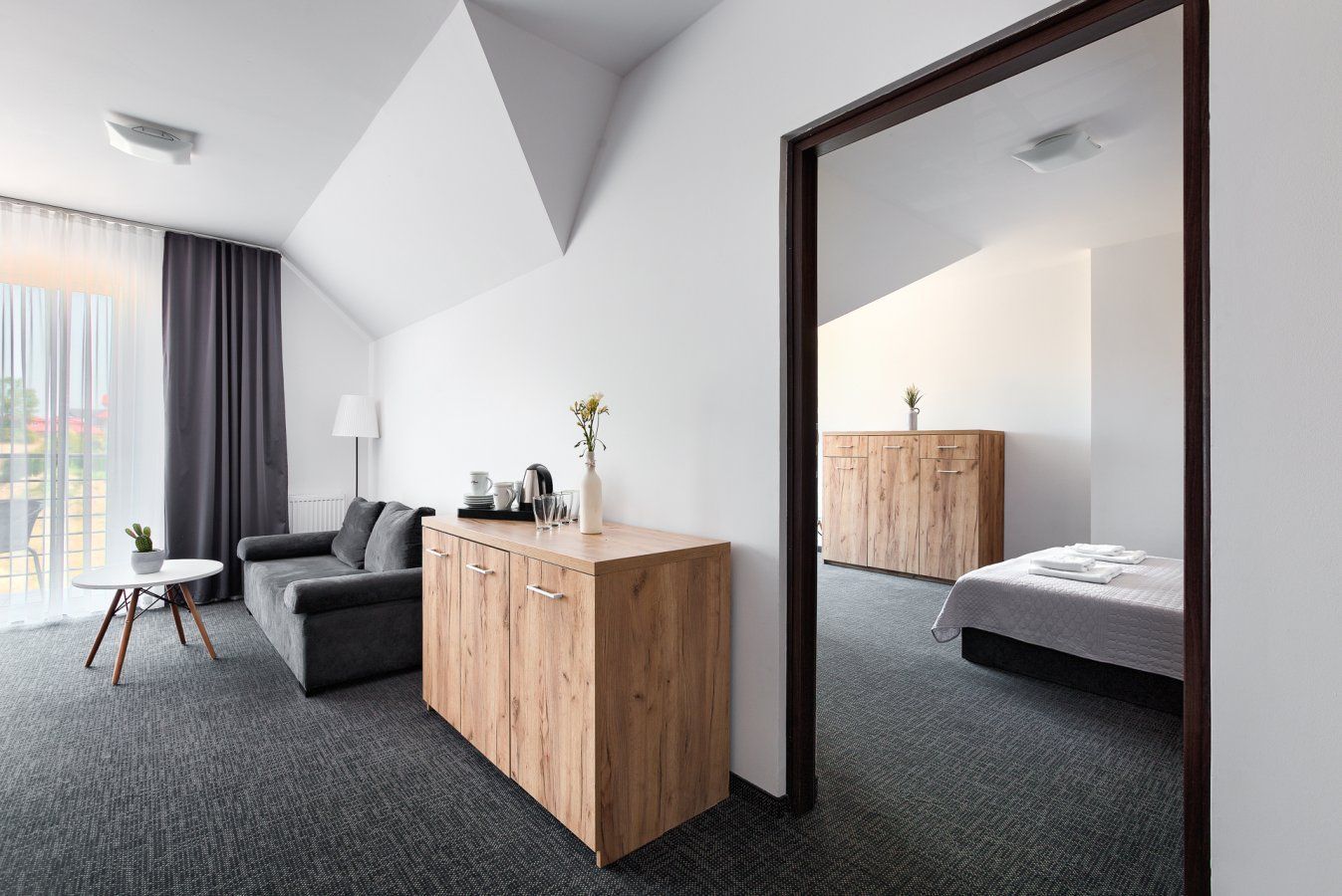 Wnętrze pokoju hotelowego z sofą, komodą i łóżkiem odbijającymi się w lustrze w drzwiach.