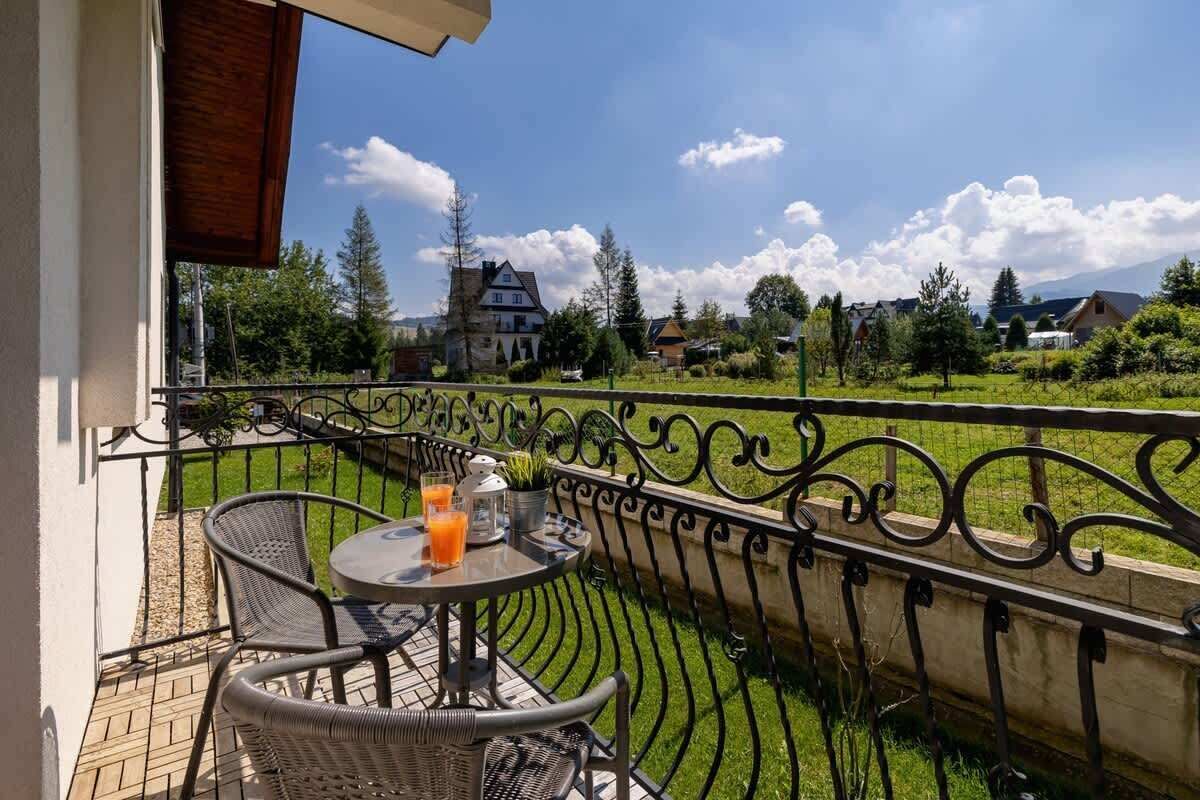 Balkon z krzesłami i stołem z kutego żelaza z widokiem na słoneczny, zielony park i budynki