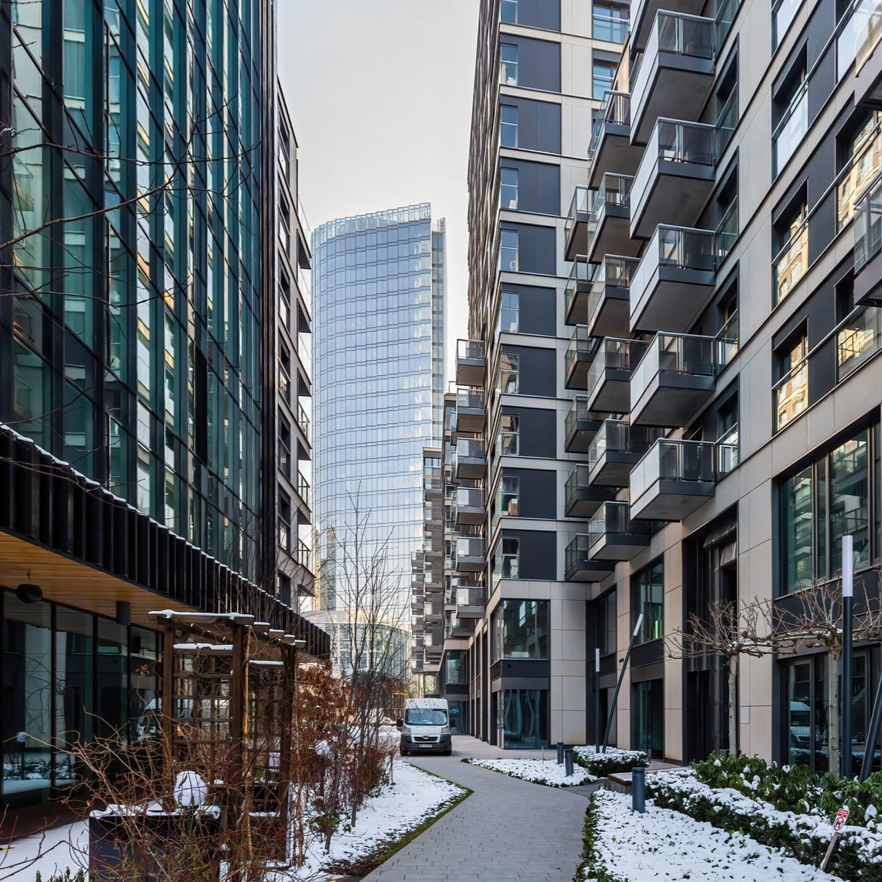 Zaśnieżona ścieżka między nowoczesnymi budynkami; w tle wysoki szklany wieżowiec.