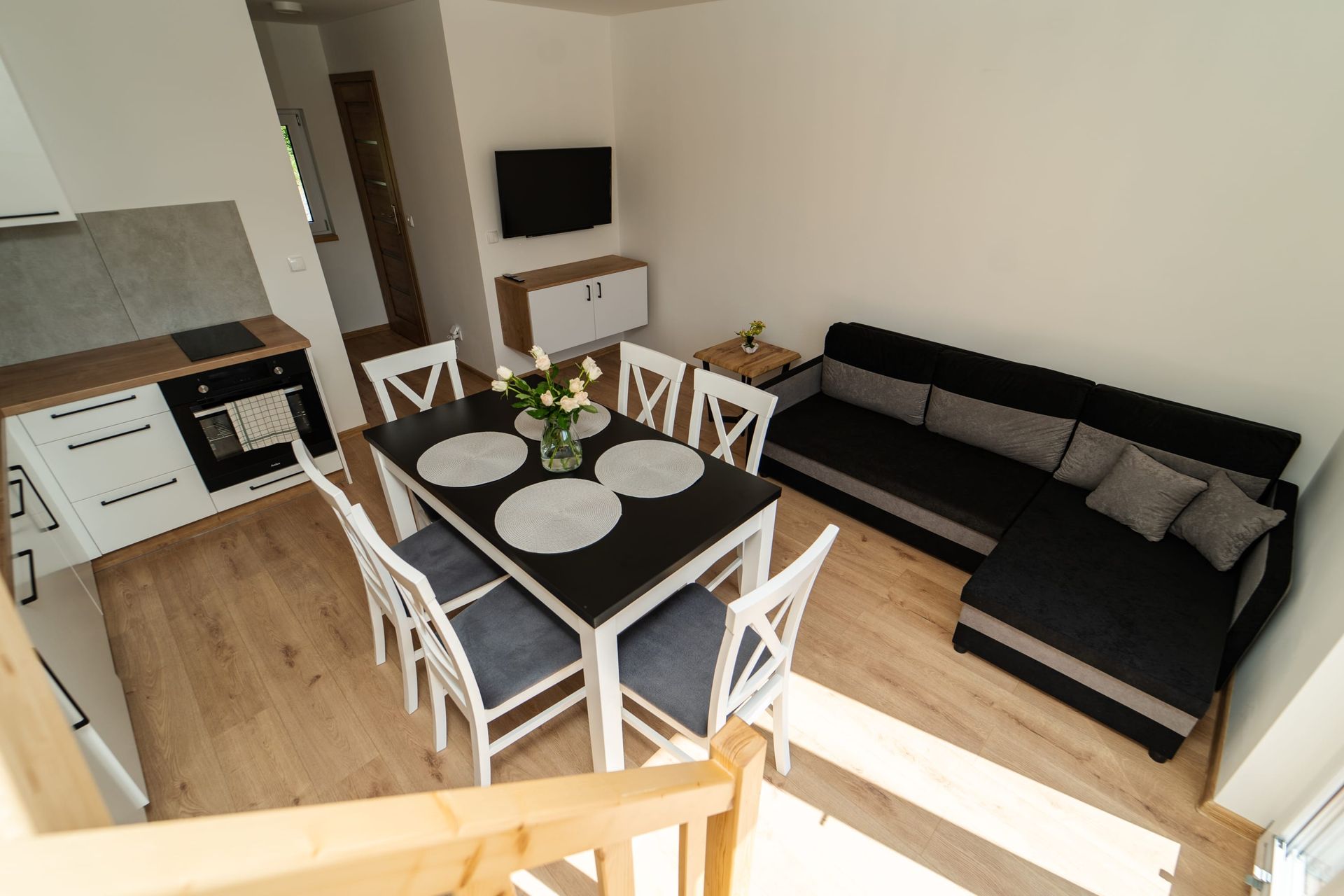 Widok wnętrza nowoczesnego salonu z jadalnią, kuchnią i kanapą. Neutralne kolory i drewniana podłoga.