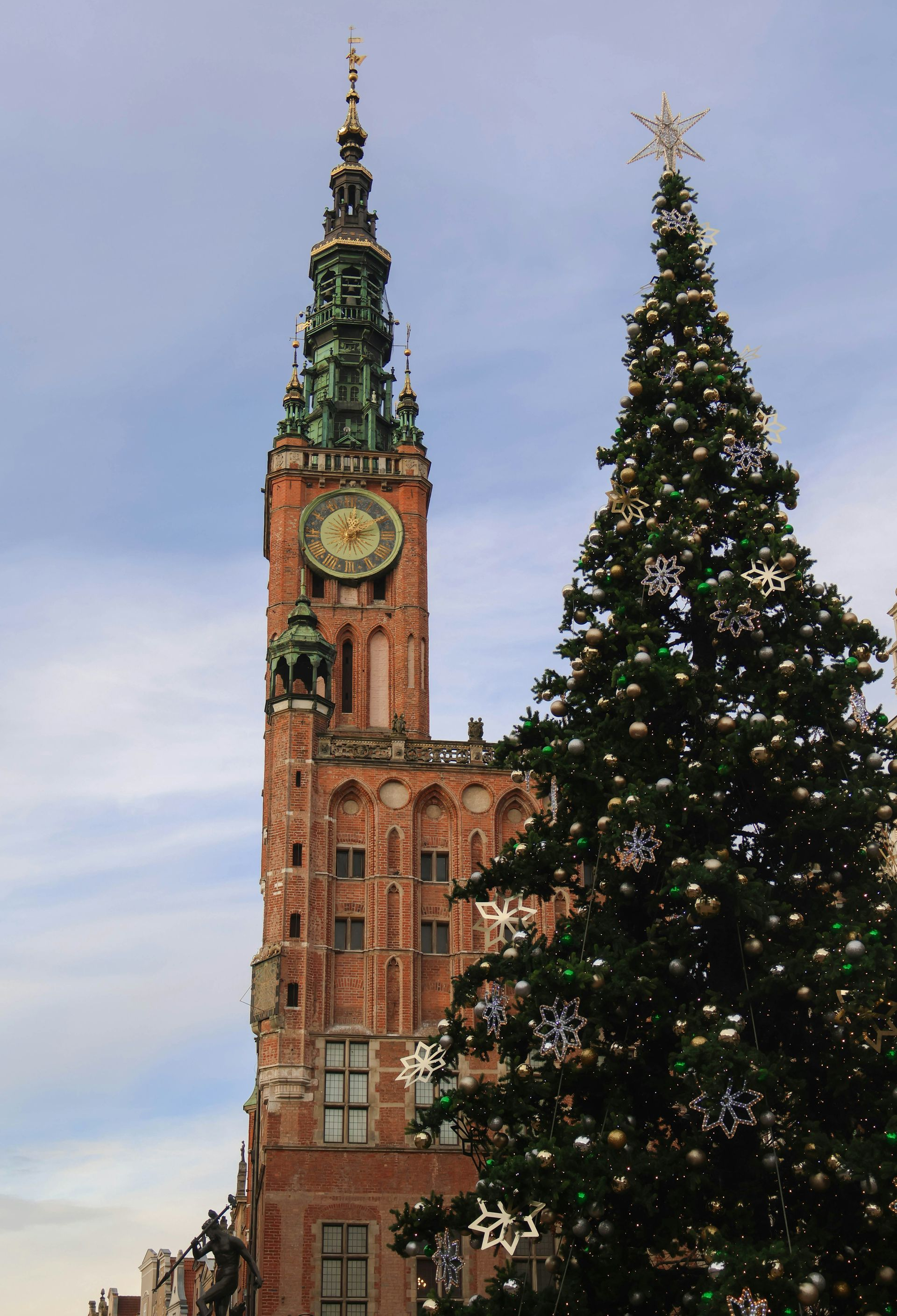 Tall brick building with a clock tower and decorated Christmas tree.