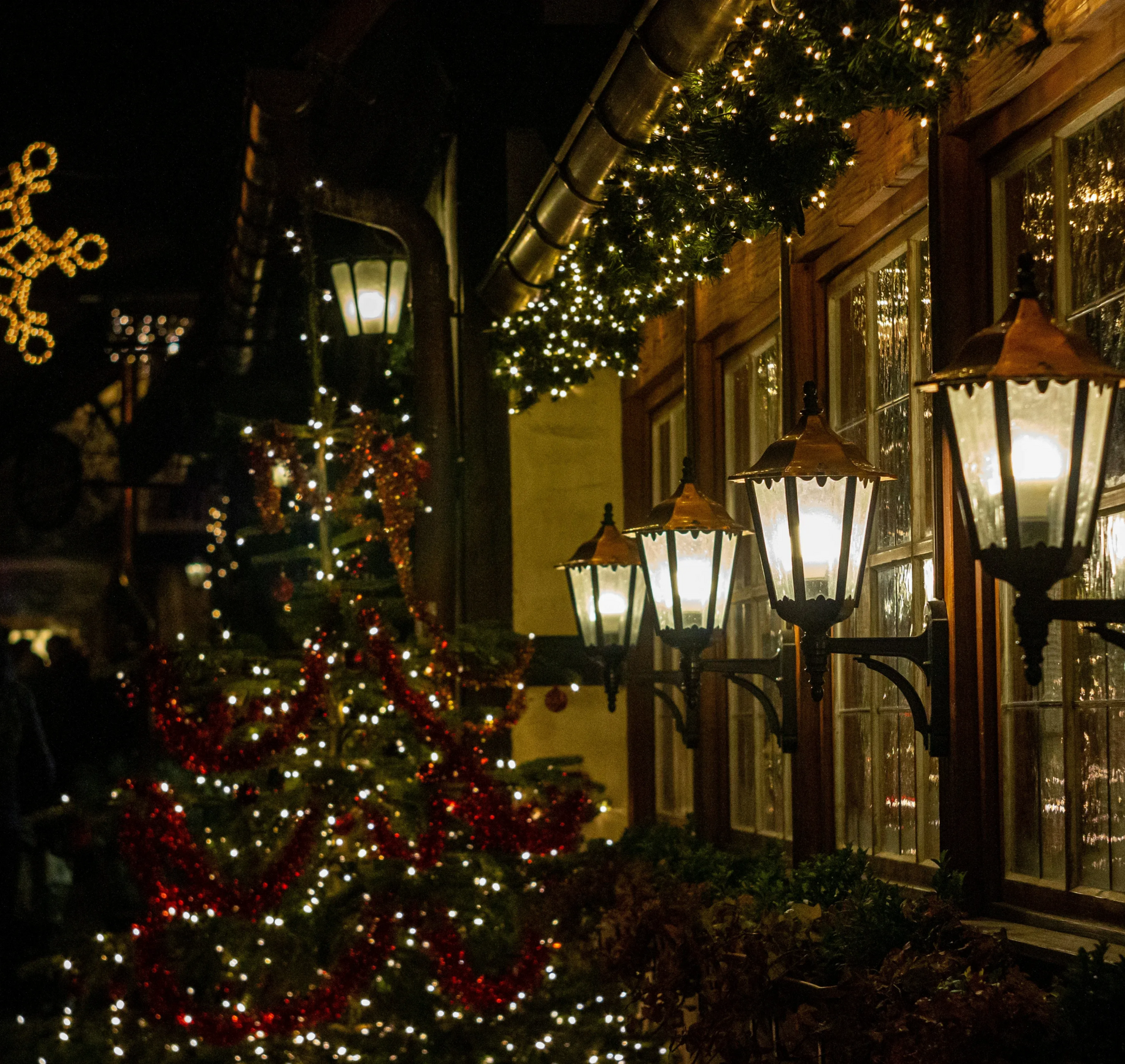 Świąteczne dekoracje na budynku nocą. Rozświetlona choinka, lampki choinkowe i latarnie uliczne tworzą świąteczną atmosferę.
