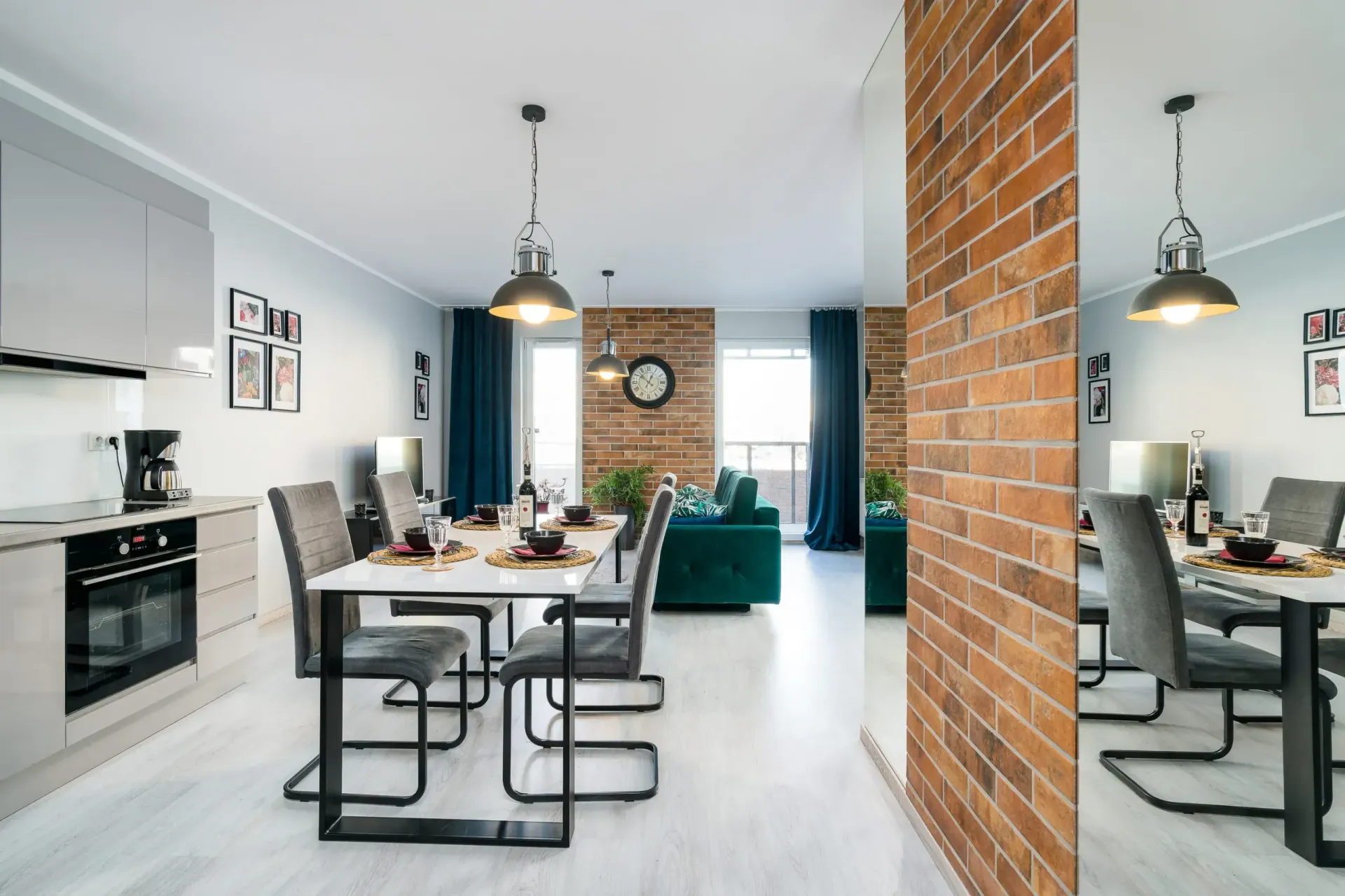 Otwarta przestrzeń dzienna z kuchnią, jadalnią i salonem. Neutralne kolory, odsłonięta cegła i nowoczesne meble.