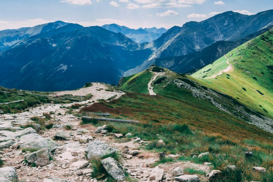 Osoba stoi na szczycie góry, w tle widać góry.