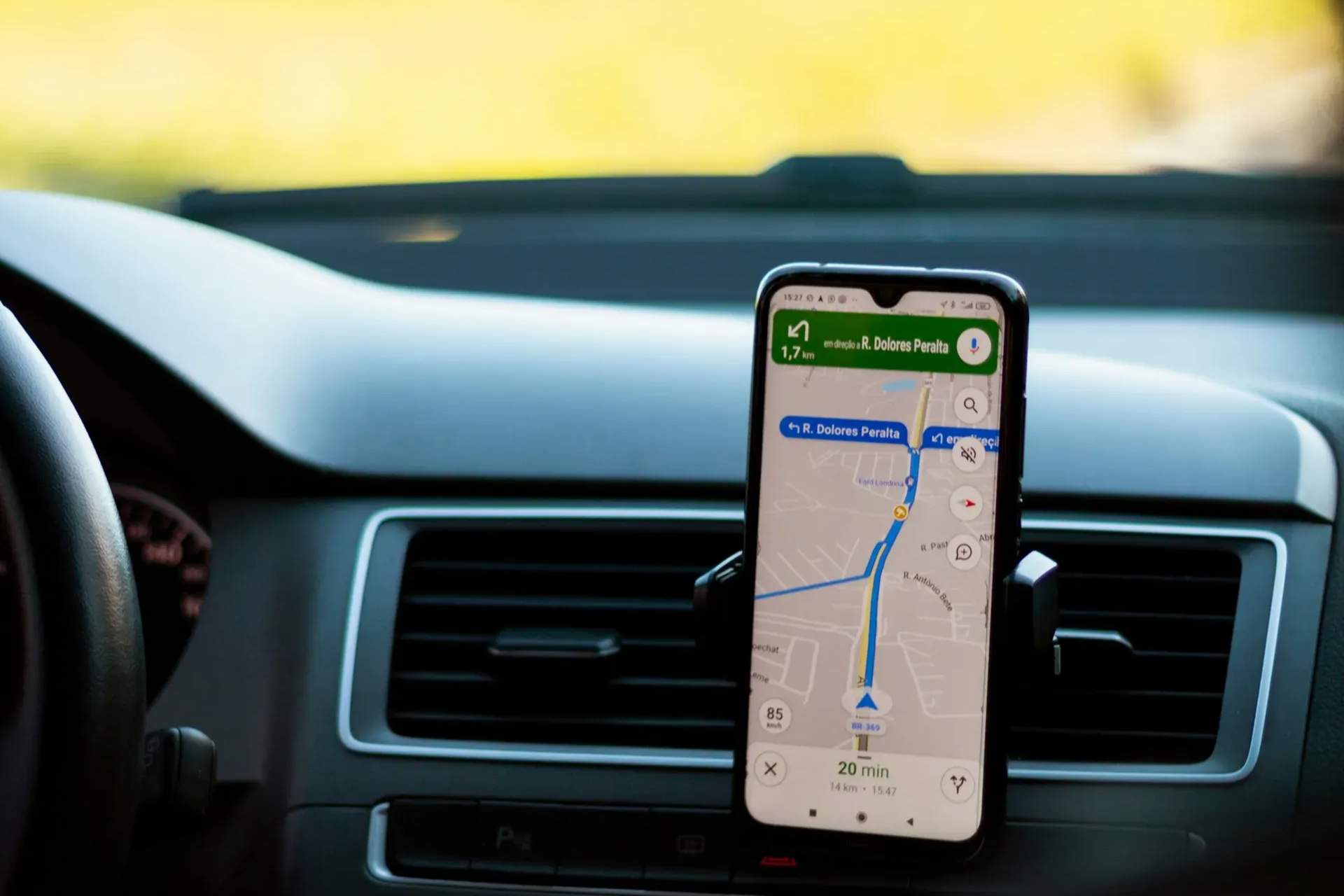 Smartphone displaying a navigation app, mounted on a car's dashboard, with a map showing the route.