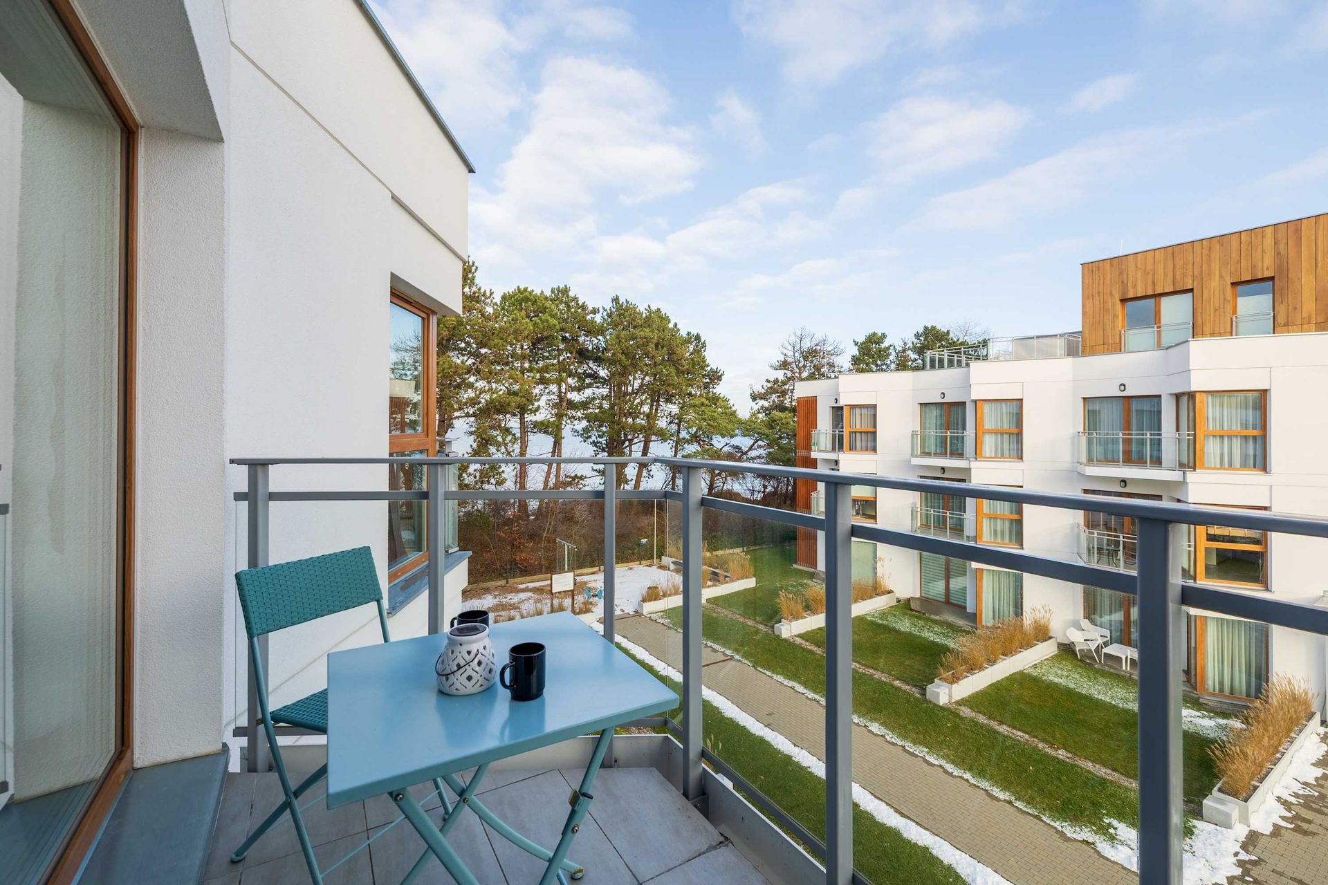 Balkon z turkusowymi krzesłami z widokiem na nowoczesny dziedziniec apartamentu i drzewa