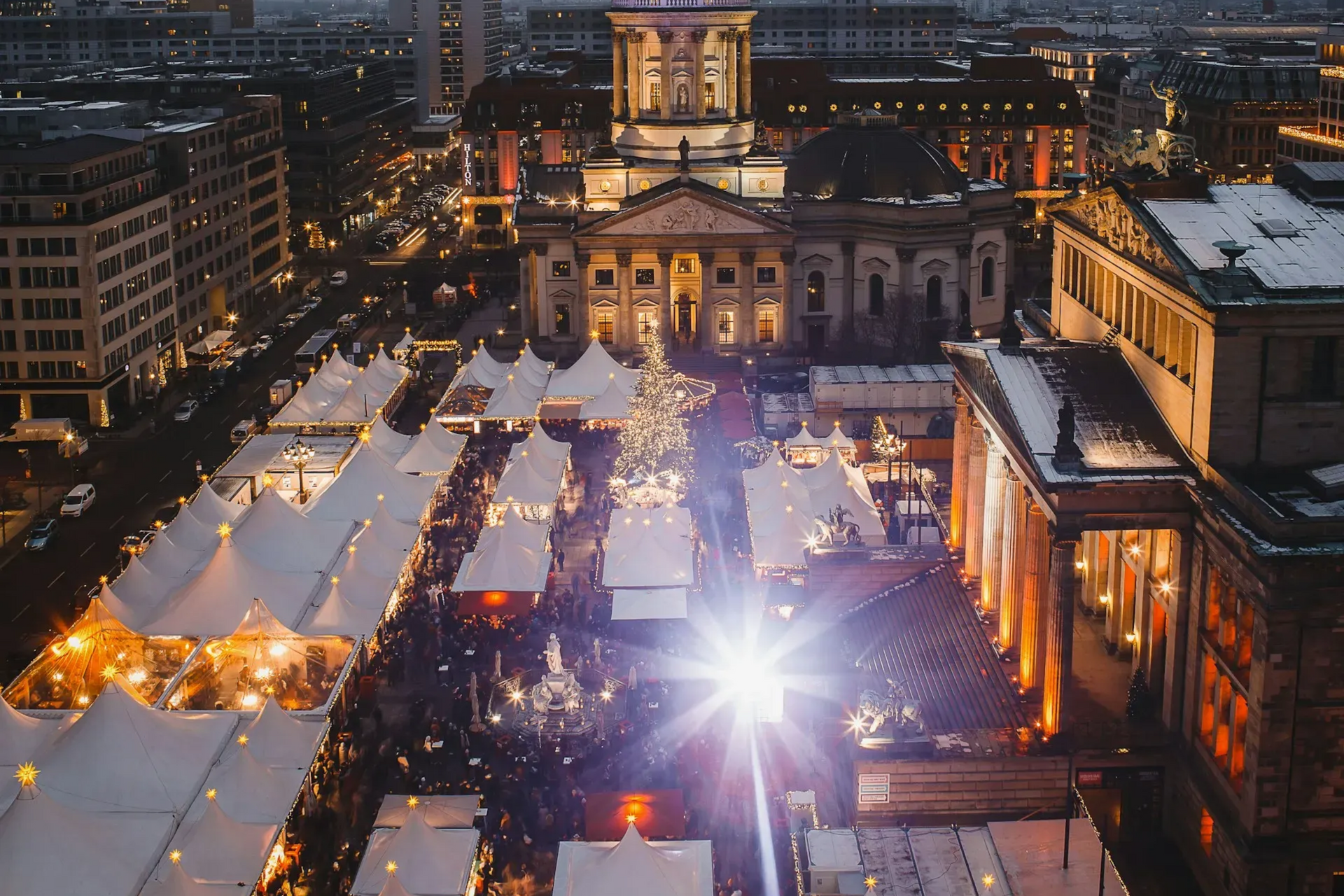 Christmas market in Berlin with lit stalls, people, and a large building in the background.