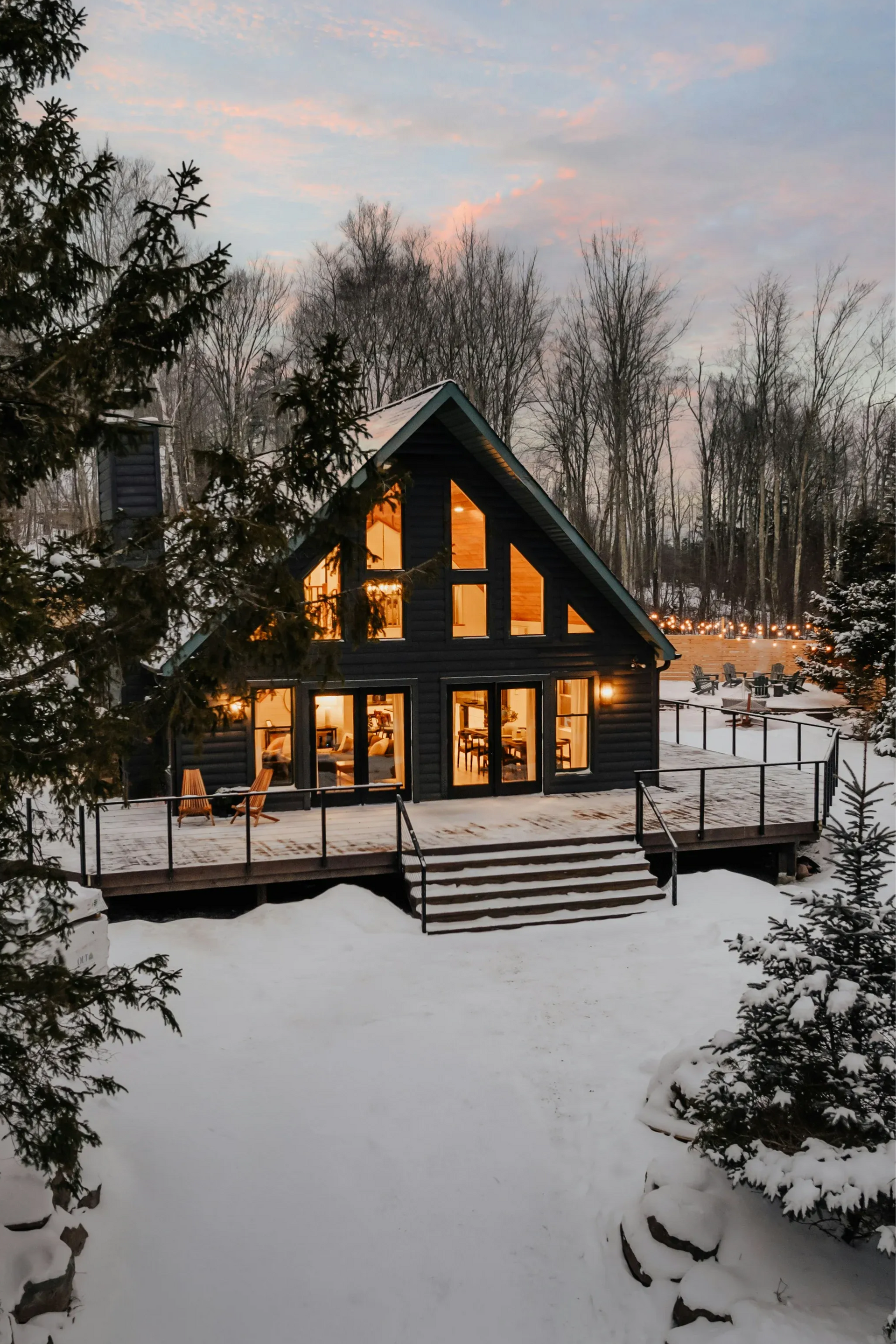 Przytulna, ciemna chata w śnieżnym krajobrazie, z włączonymi światłami w środku.