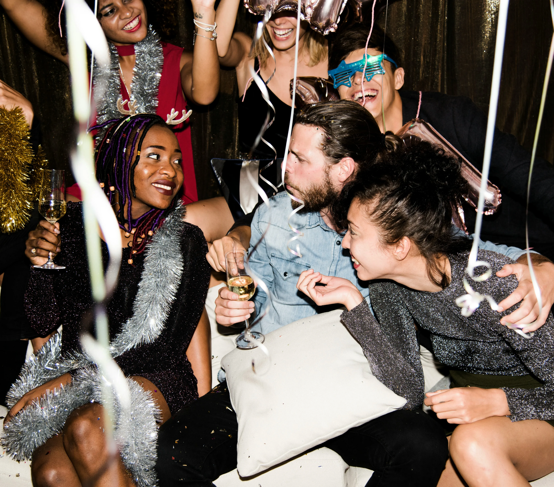 Ludzie na imprezie, niektórzy trzymają w rękach drinki, z serpentynami i światełkami.