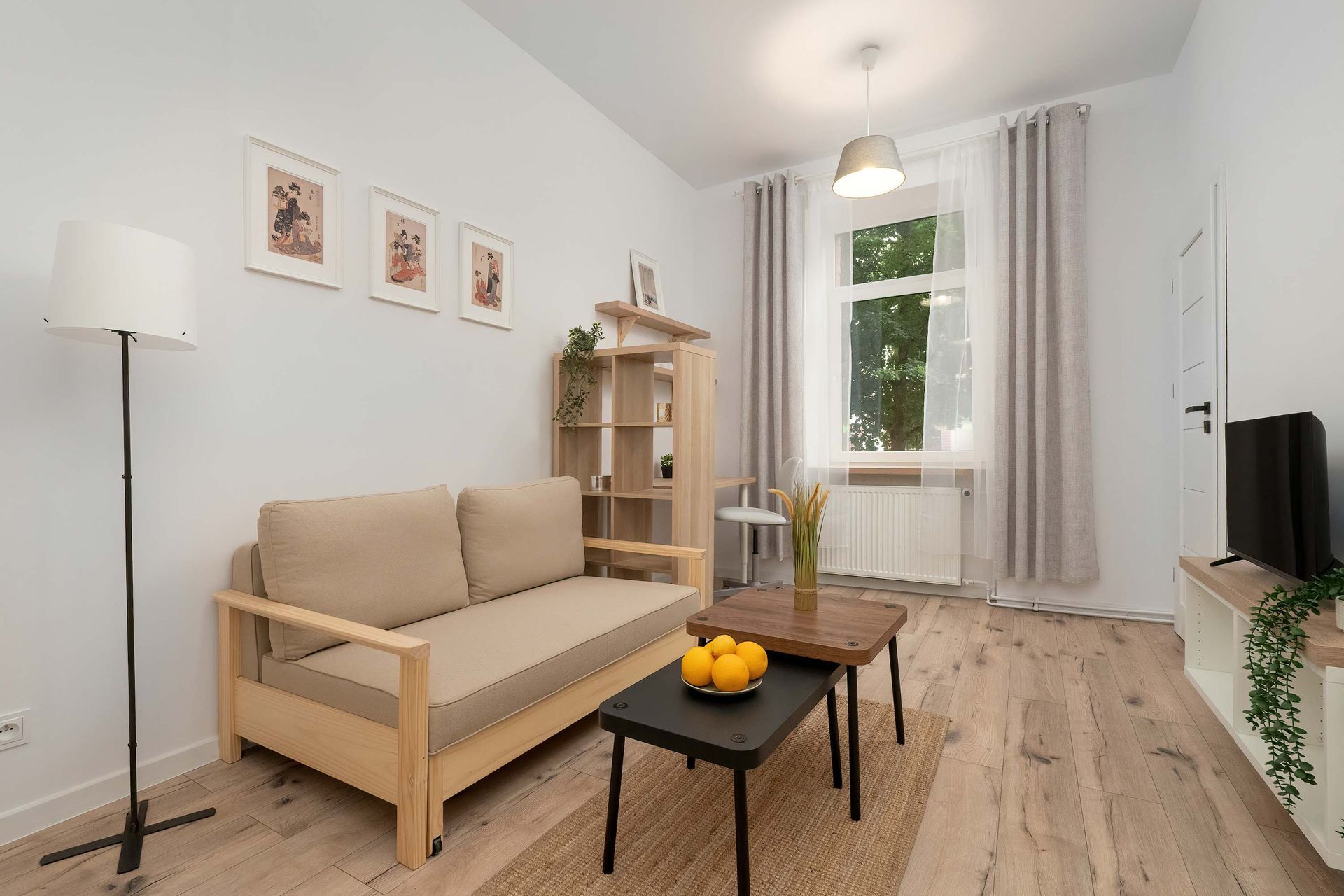 Jasny salon z beżową sofą, czarnym i drewnianym stolikiem kawowym, drewnianą półką i oknem z zasłonami.