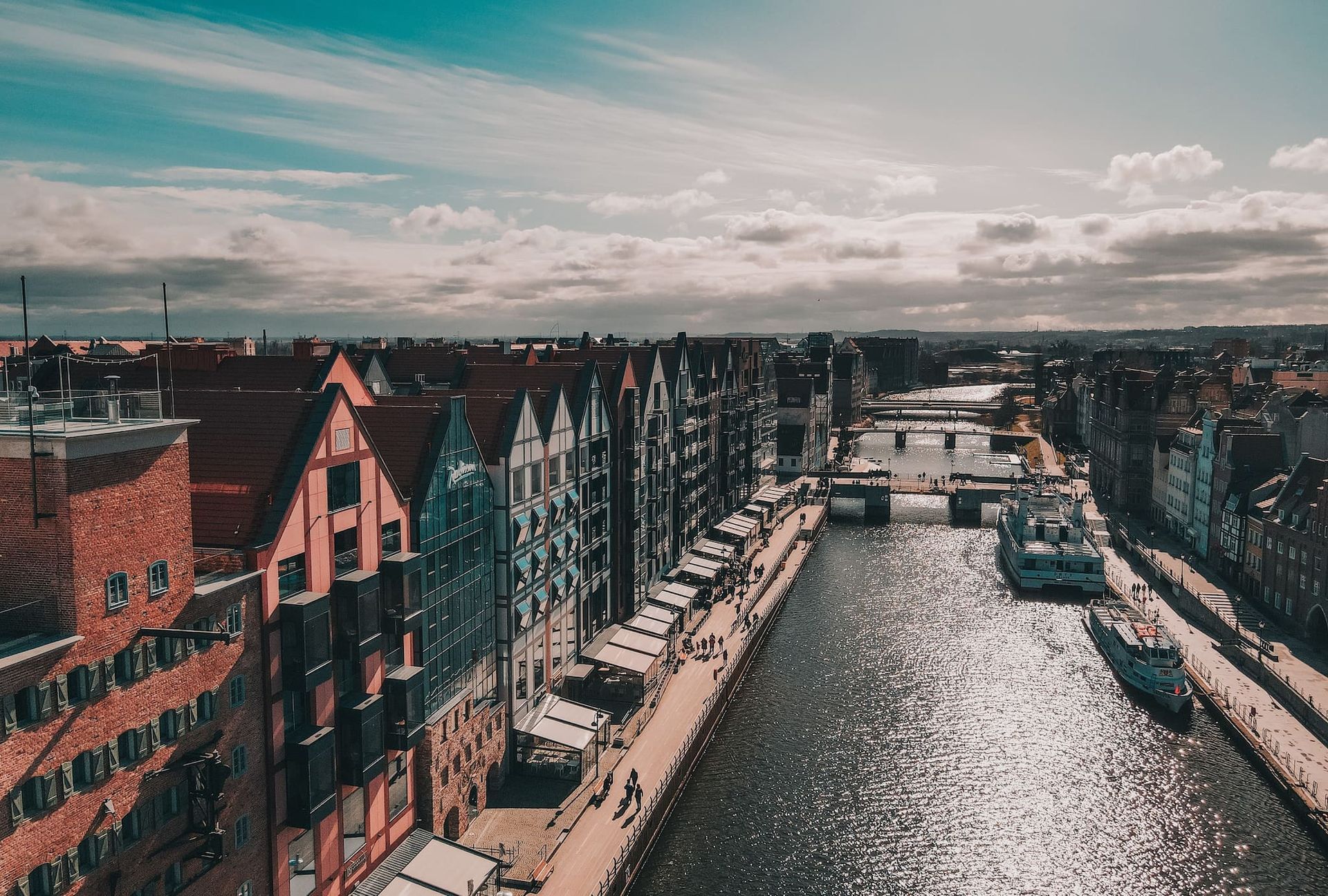 Widok na kanał w Gdańsku, w Polsce, otoczony kolorowymi budynkami i łodziami, pod częściowo zachmurzonym niebem.
