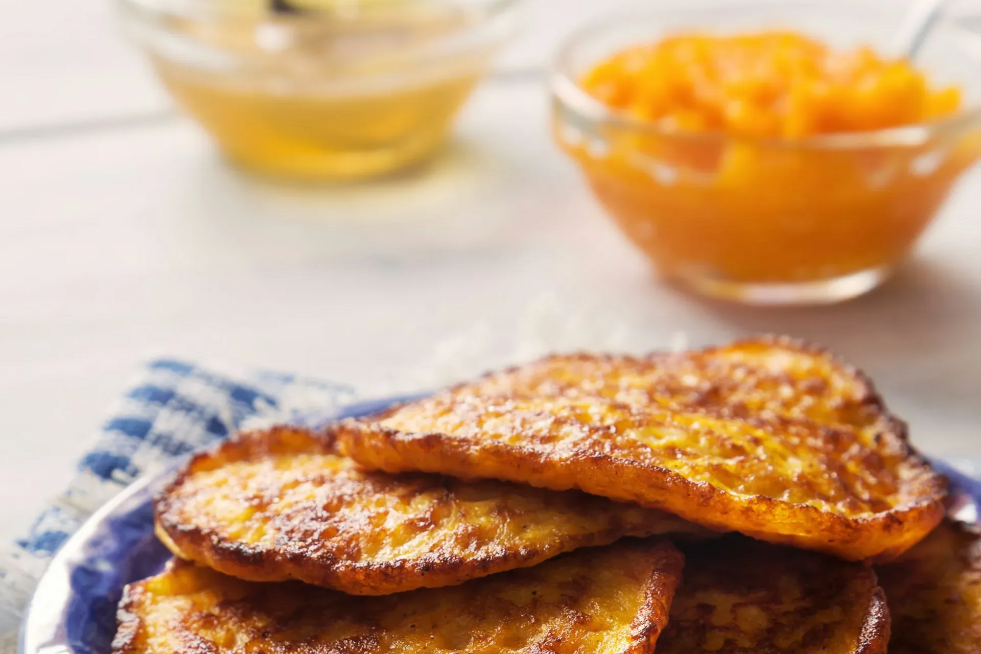 Golden French toast on a blue plate, with honey and orange jam in the background.