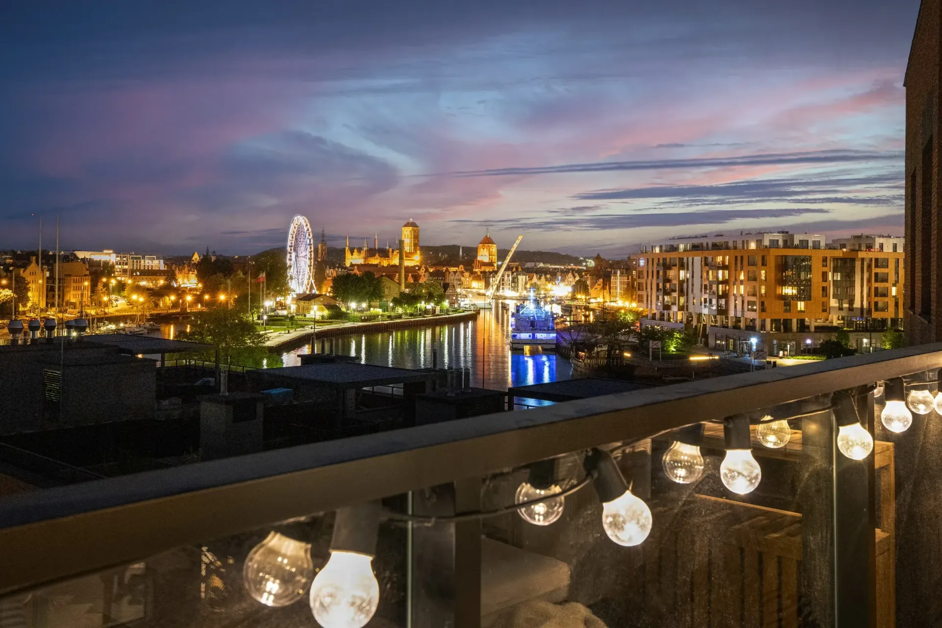 Sypialnia z czarną ścianą, łóżkiem i ozdobnymi lampami wiszącymi. Nad wezgłowiem łóżka wiszą dwa oprawione zdjęcia.