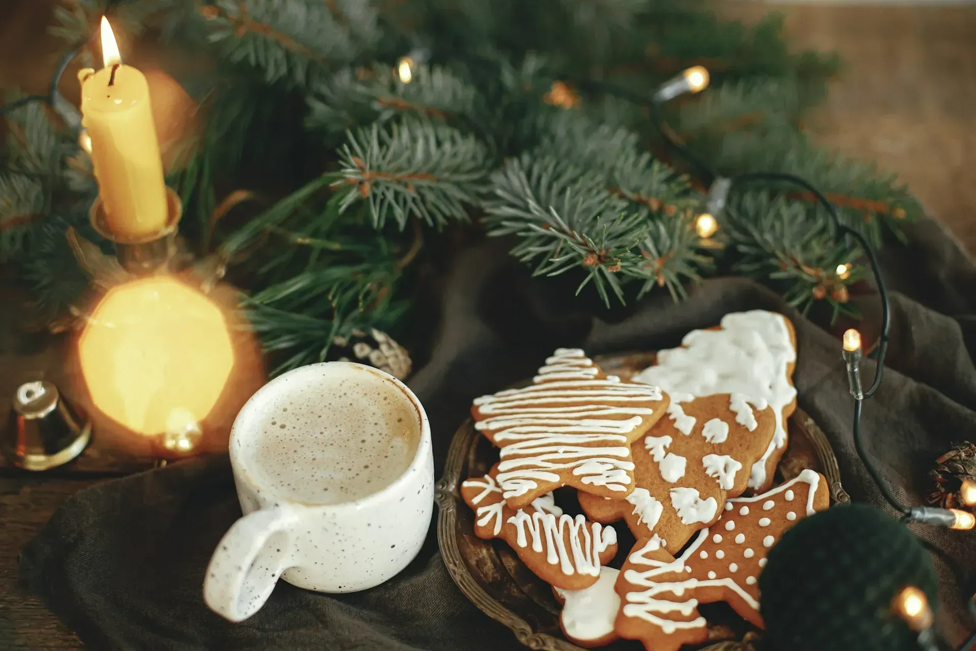 Cup of coffee with gingerbread cookies, lit candle, and Christmas tree decorations.