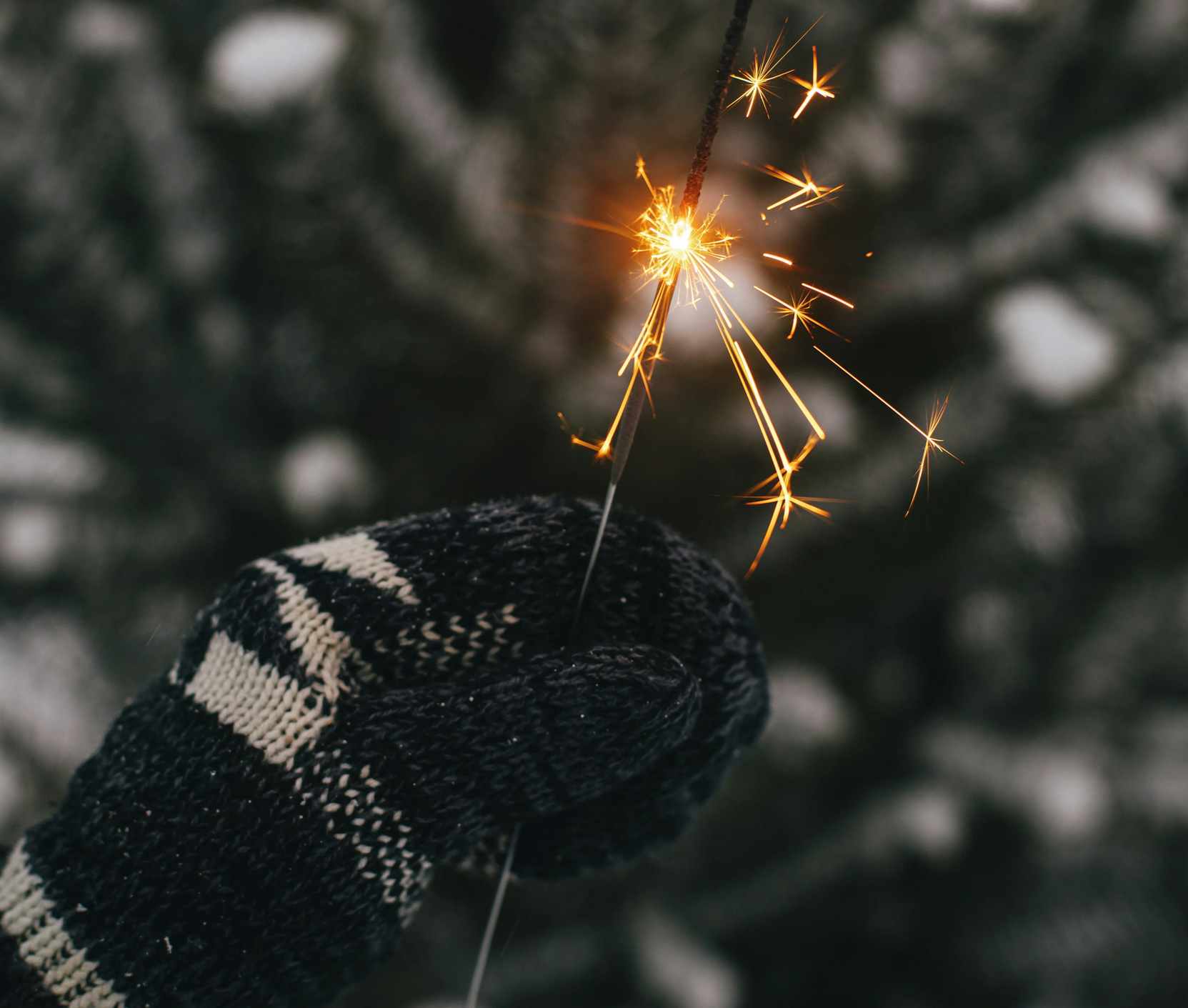 Dłoń w rękawiczce trzymająca zimny ogień z iskrami na rozmytym, ciemnozielonym tle.