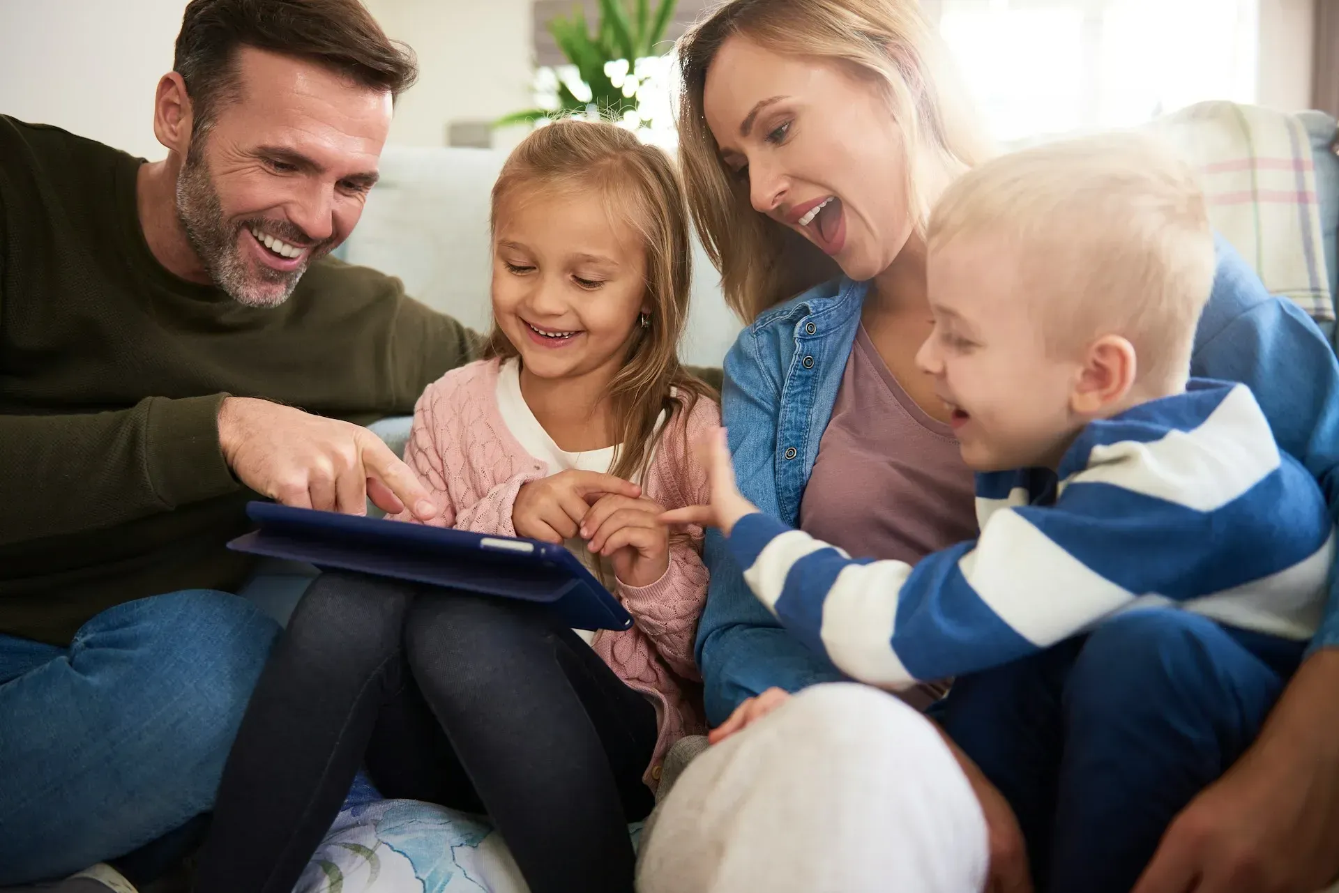 Family sitting on a couch looking at a tablet, smiling and laughing.