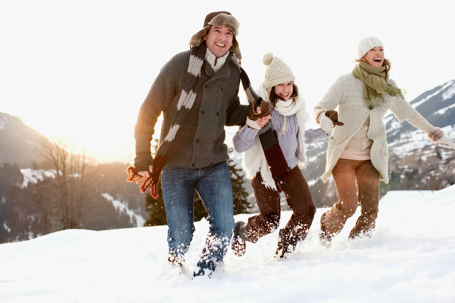 Family running in snowy field, mountains in background, sunny day.
