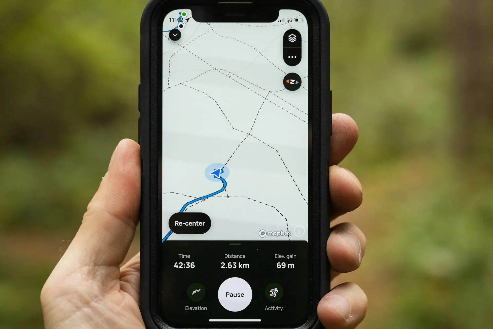A hand holds a phone displaying a map with a blue line indicating a route; outdoors.