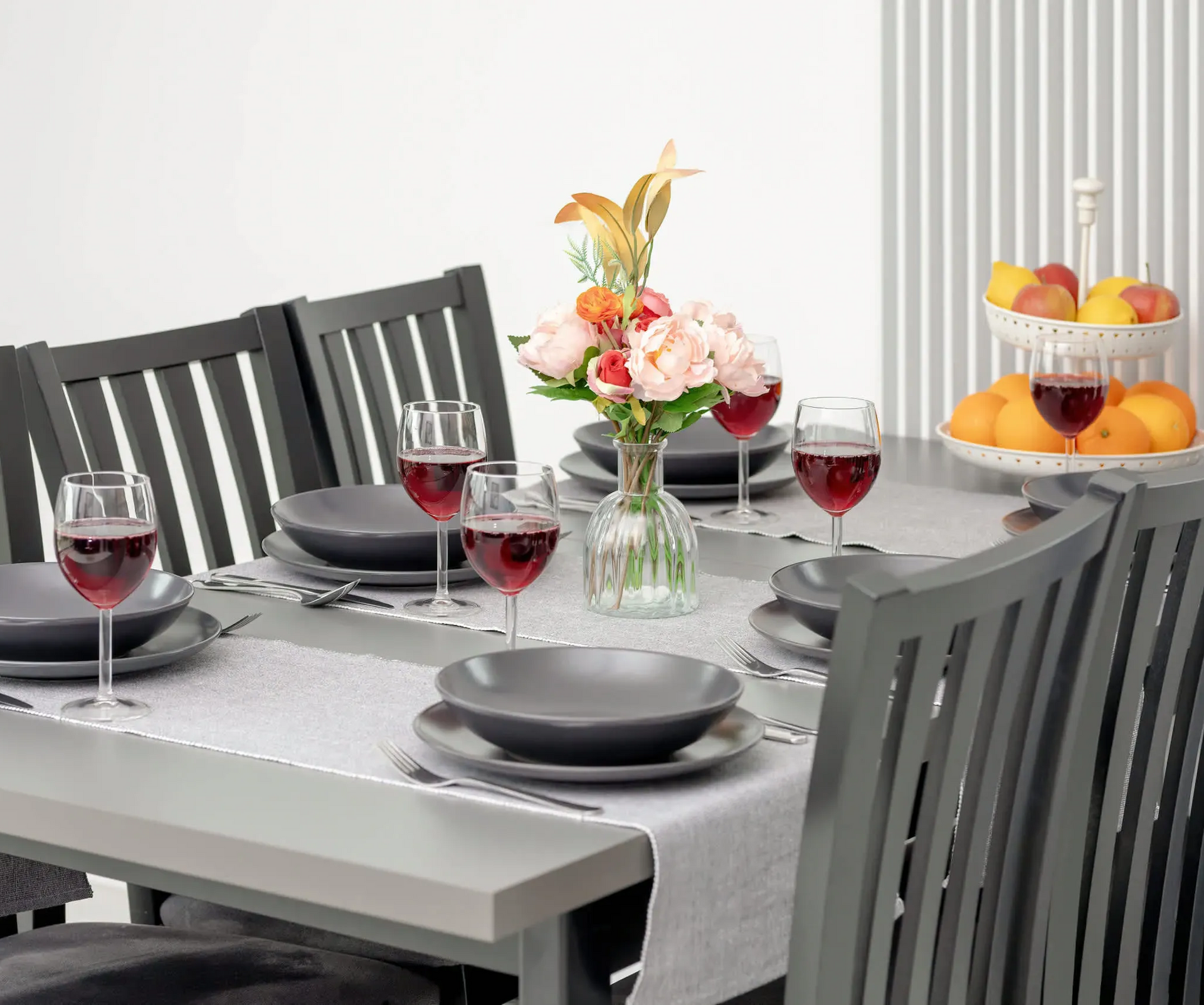 Stół jadalny zastawiony talerzami, szklankami i kwiatami; krzesła wokół jasnoszarego stołu.