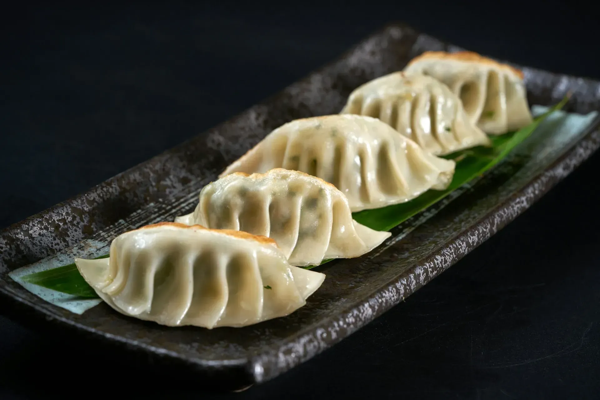 Dumplings on a rectangular plate, arranged on a green leaf. Dark, textured surface.