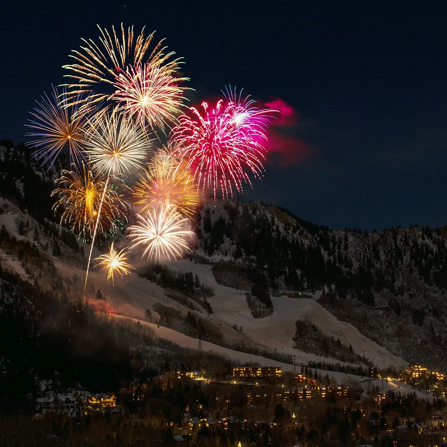Pokaz sztucznych ogni nad ośnieżonymi górami i rozświetlone miasto nocą.