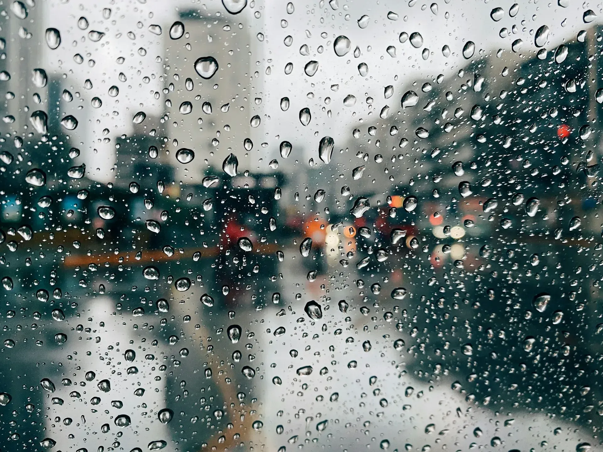 Raindrops on a window obscure a blurry cityscap, buildings, street lights, and traffic are visible.