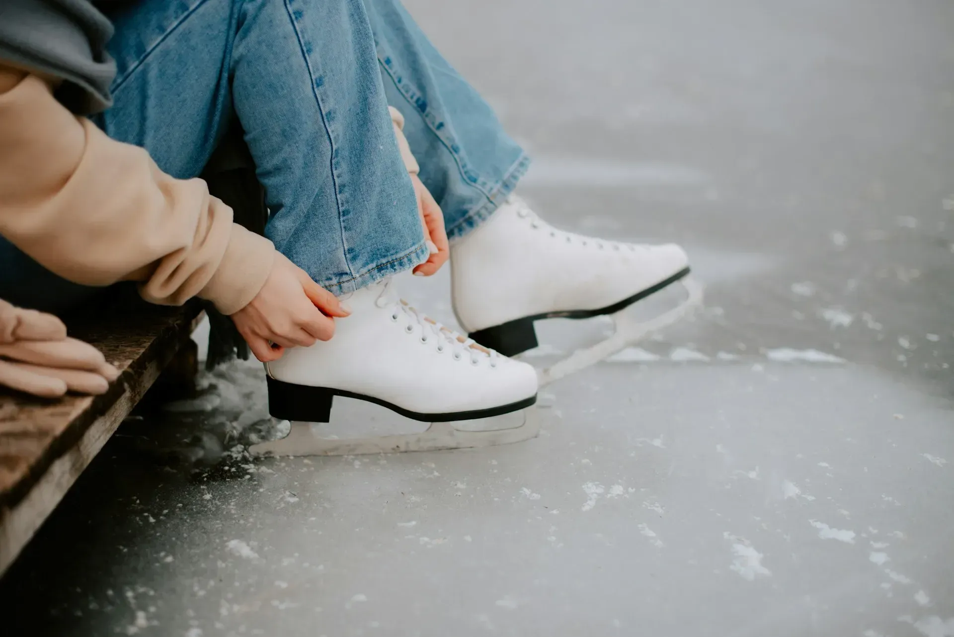 Person tying white ice skates, sitting on edge of ice.