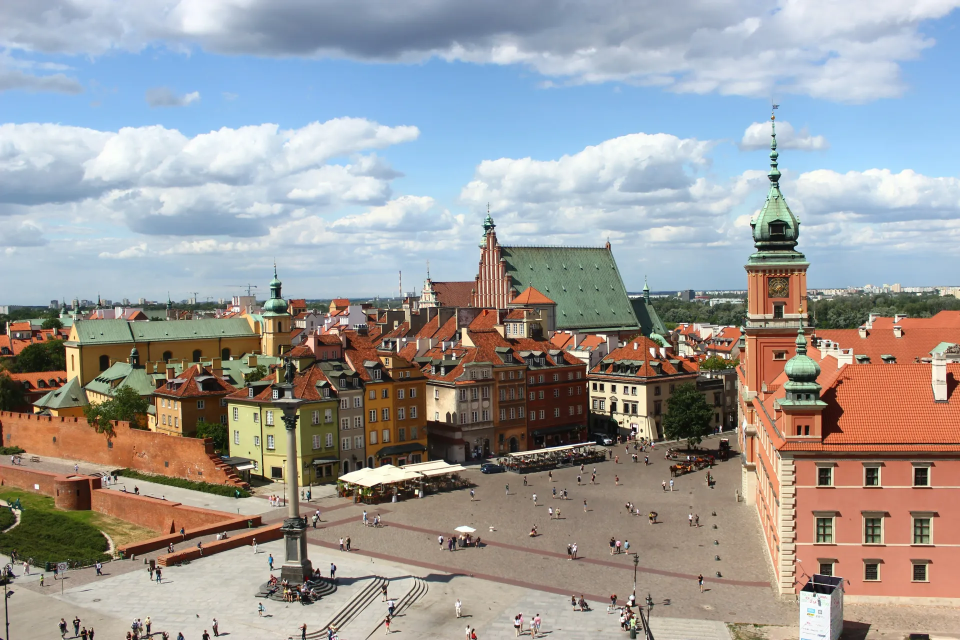 Warsaw, Poland Old Town Square with red-roofed buildings, a central plaza, and a blue sky with clouds.