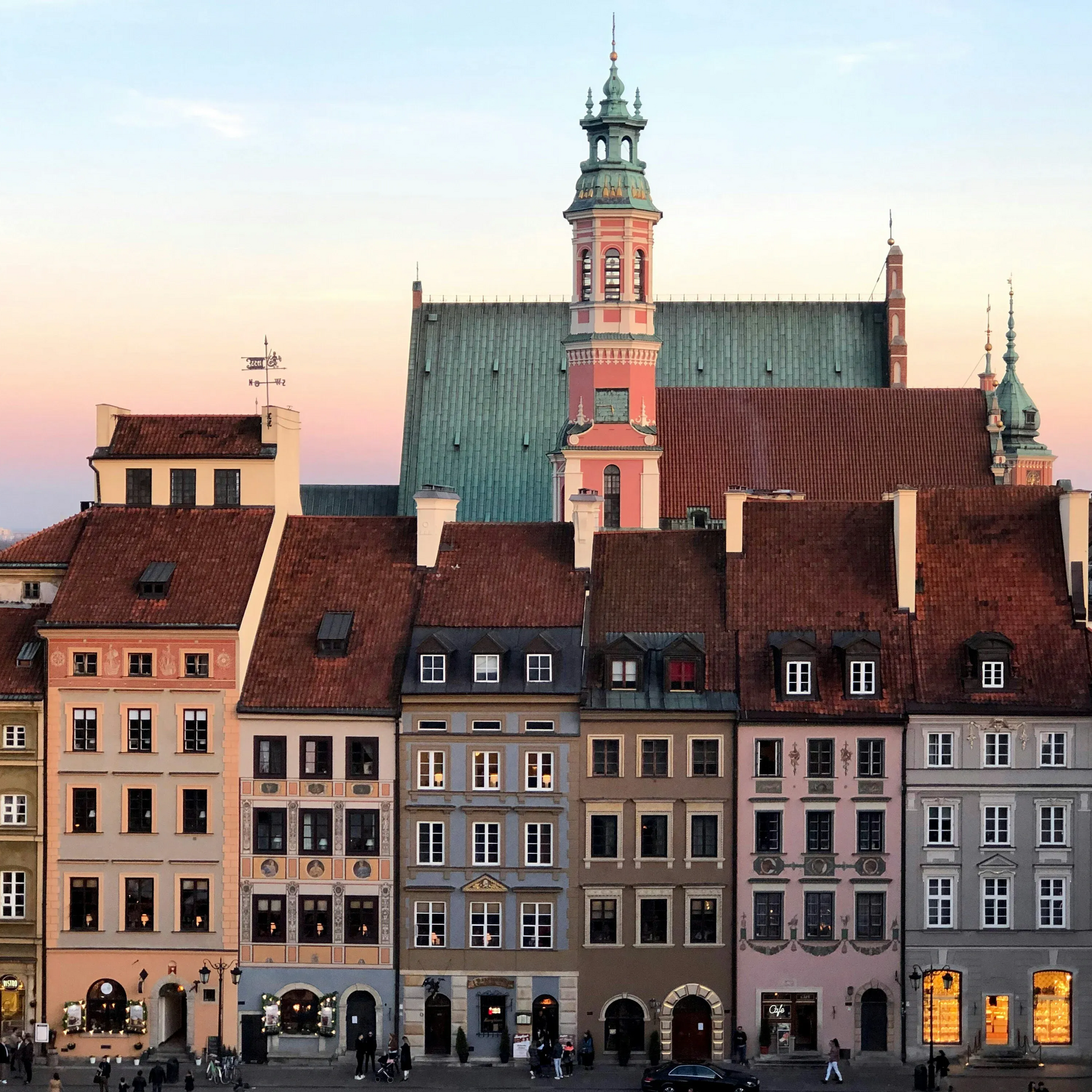 Rząd kolorowych budynków z wysoką wieżą w tle, na tle kolorowego zachodu słońca. Stare Miasto w Warszawie.
