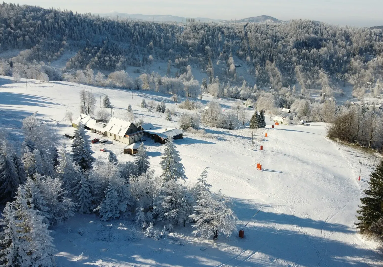 Pokryty śniegiem krajobraz z drzewami, budynkiem i stokiem narciarskim.