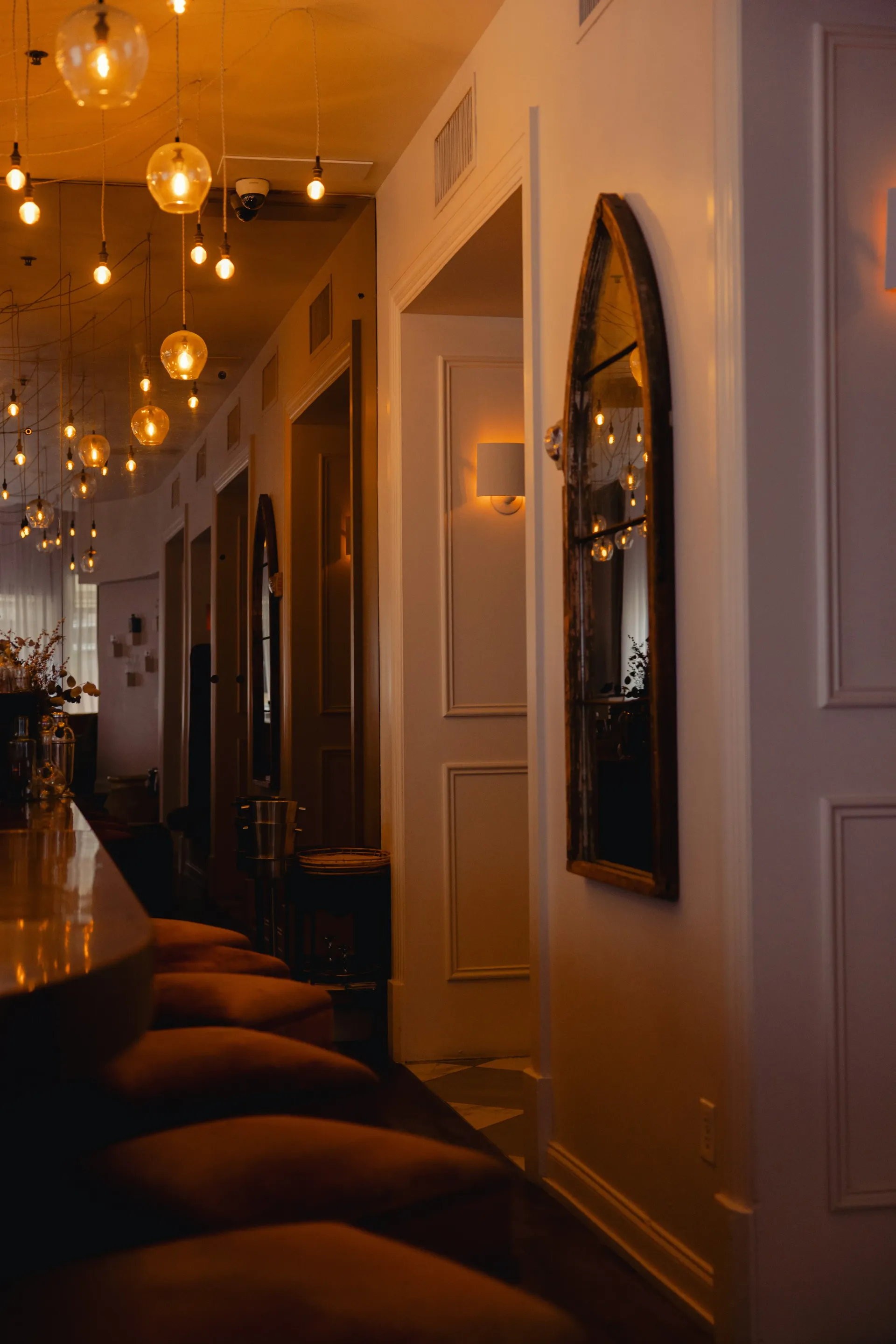 Wnętrze z blatem, aksamitnymi krzesłami, lustrem w kształcie łuku i ciepłym oświetleniem.