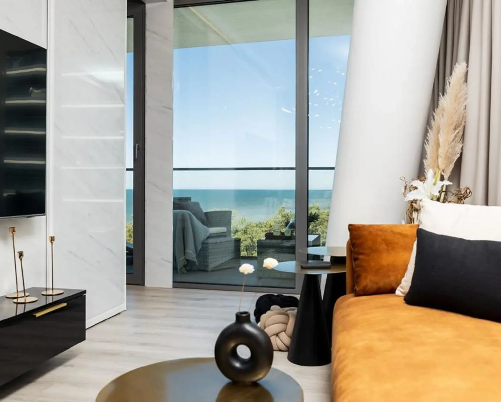 Salon z widokiem na ocean, pomarańczowa sofa, czarny wazon i nowoczesny wystrój.