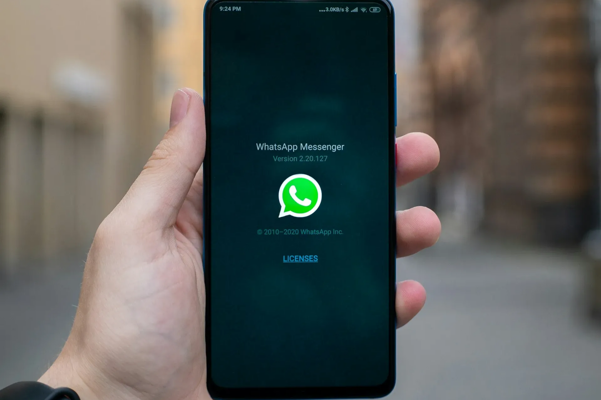 Hand holding a smartphone displaying the WhatsApp Messenger logo on the screen.