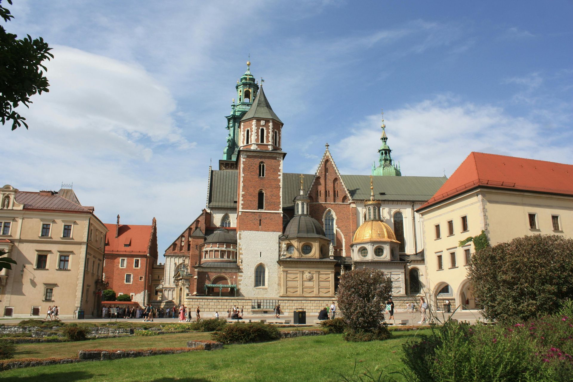 Zamek Królewski na Wawelu w Krakowie, z czerwoną cegłą i złotą kopułą na tle błękitnego nieba.