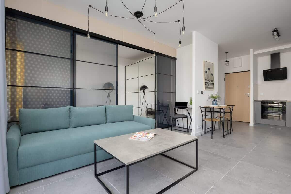 Salon z niebieską sofą, szarym stolikiem kawowym, szklaną ścianą i jadalnią.