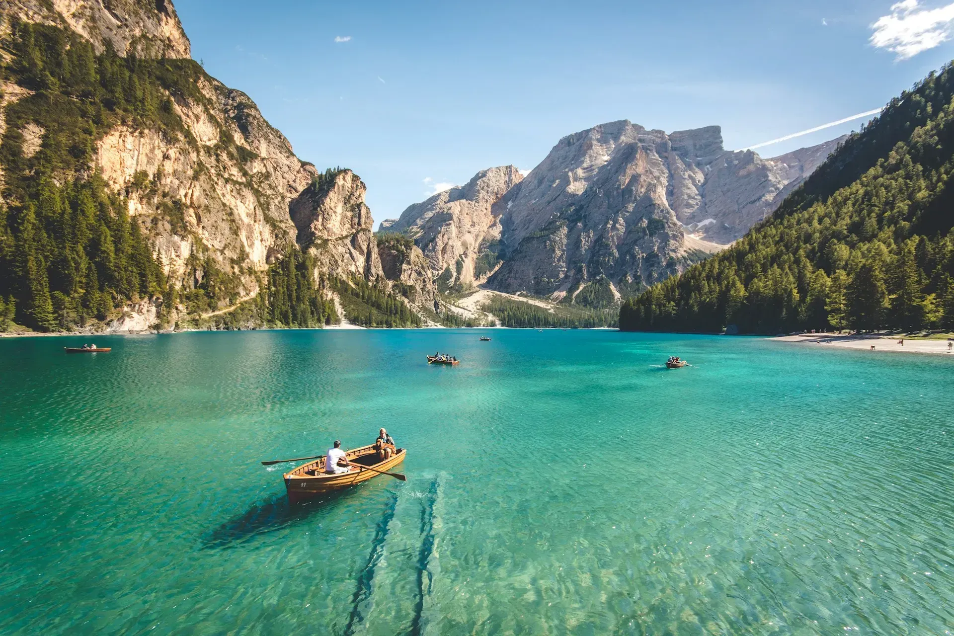 A turquoise lake with boats, surrounded by mountains and trees under a clear sky.