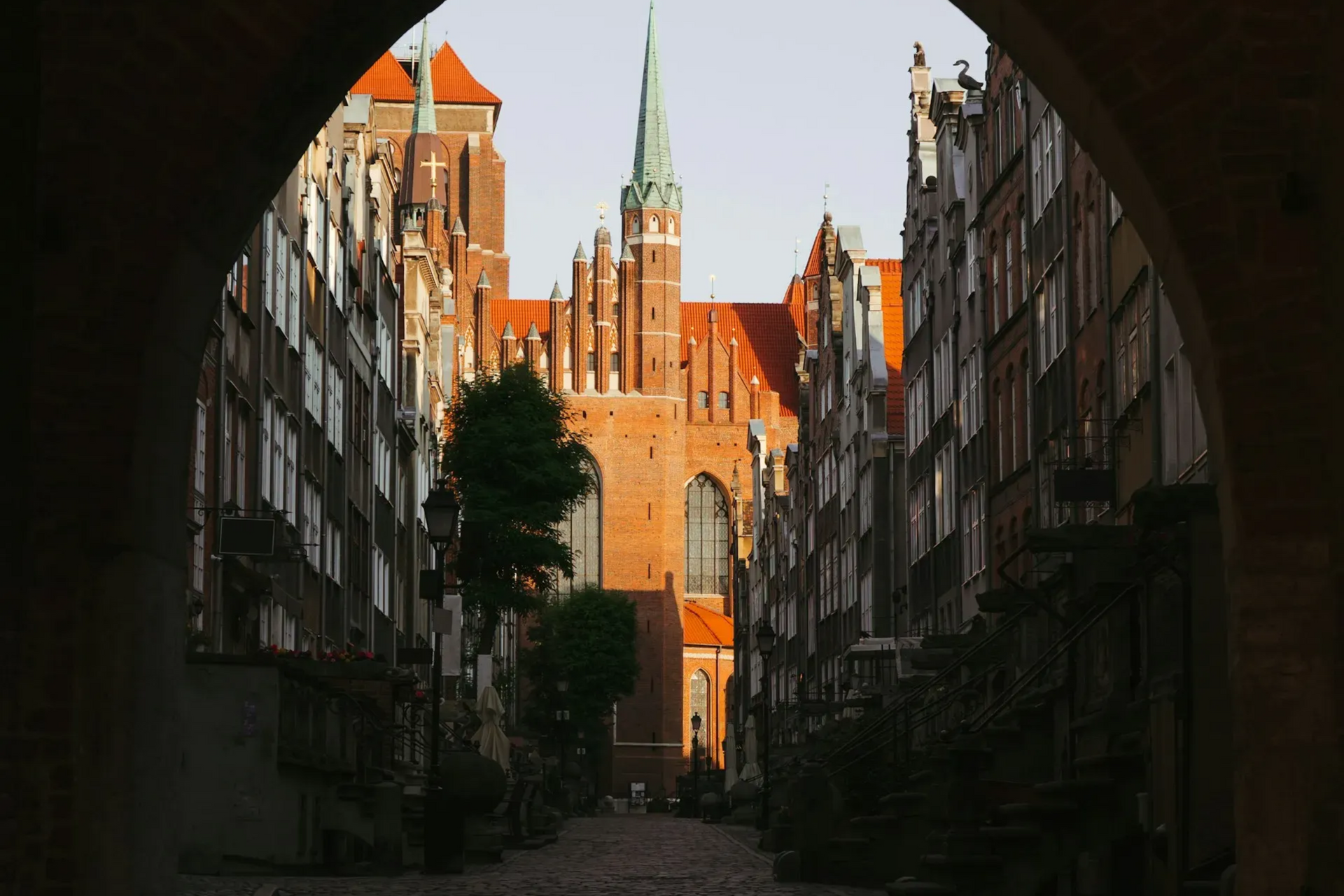 View of St. Mary's Church in Gdańsk, Poland, framed by an archway, with brick buildings lining the street.