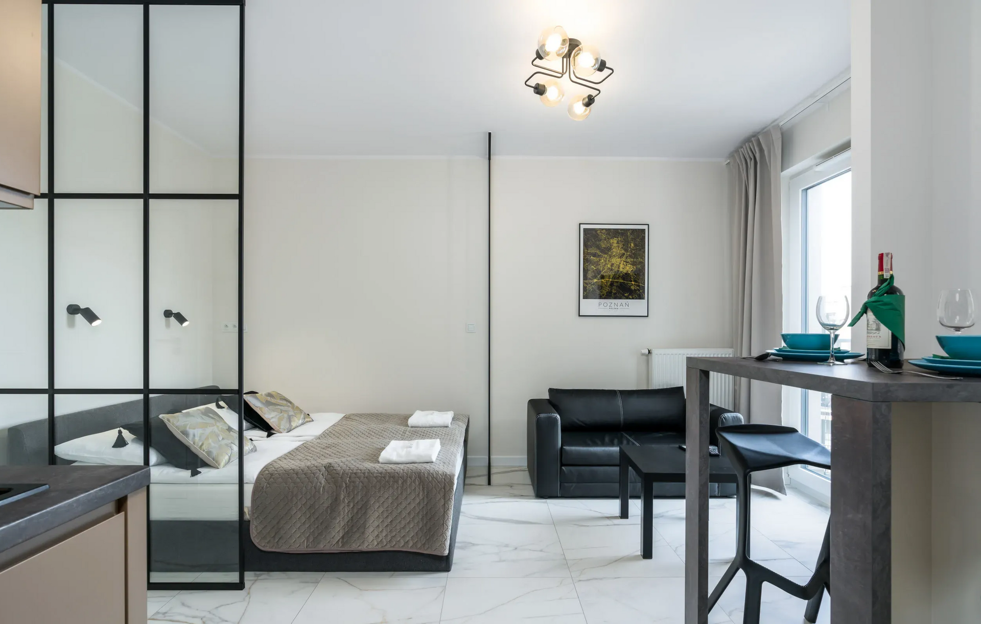 Apartament typu studio z łóżkiem, czarną sofą, blatem jadalnym i szklaną ścianą.