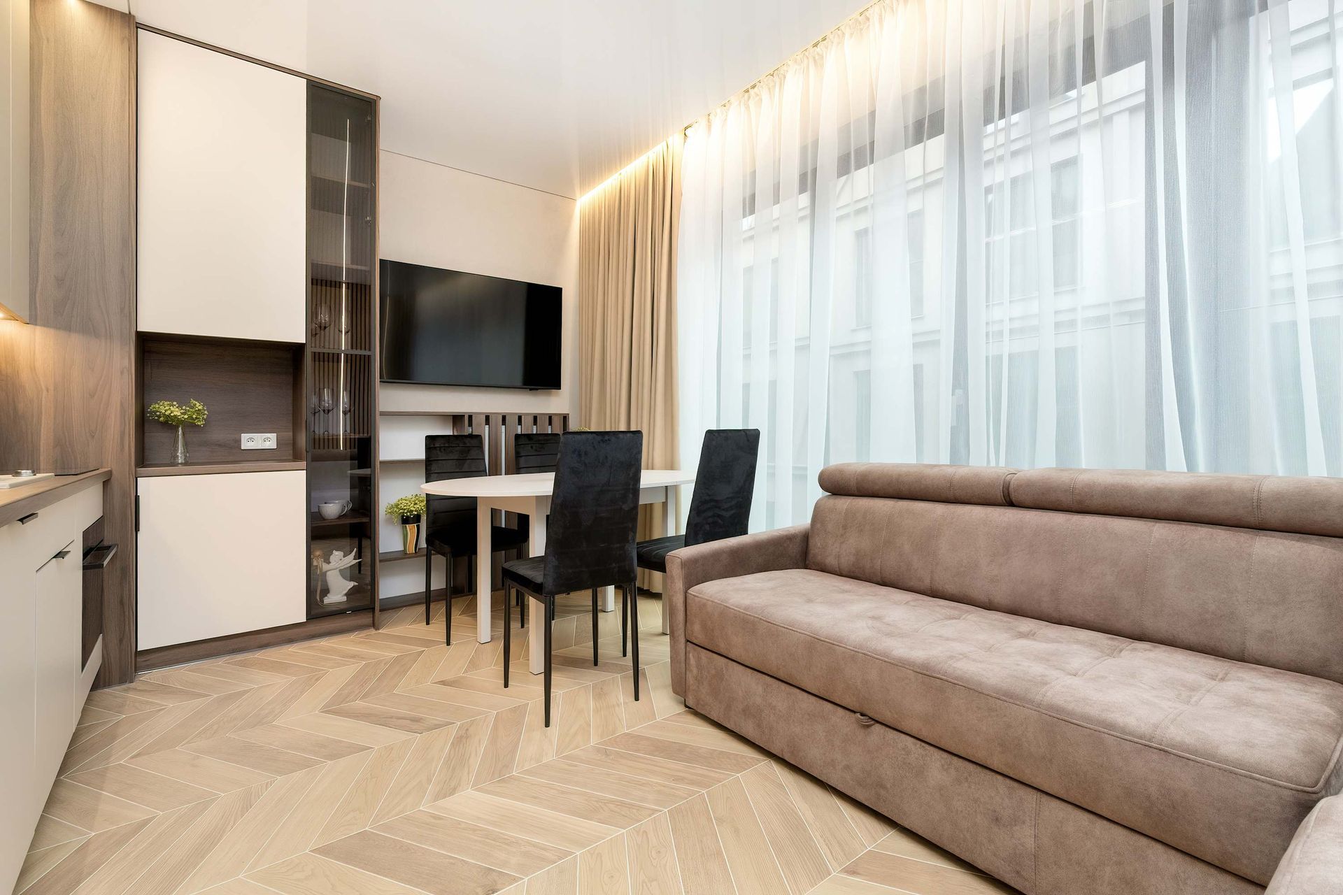 Nowoczesne wnętrze apartamentu z jasną drewnianą podłogą, białymi i brązowymi szafkami oraz sofą w stonowanych kolorach.